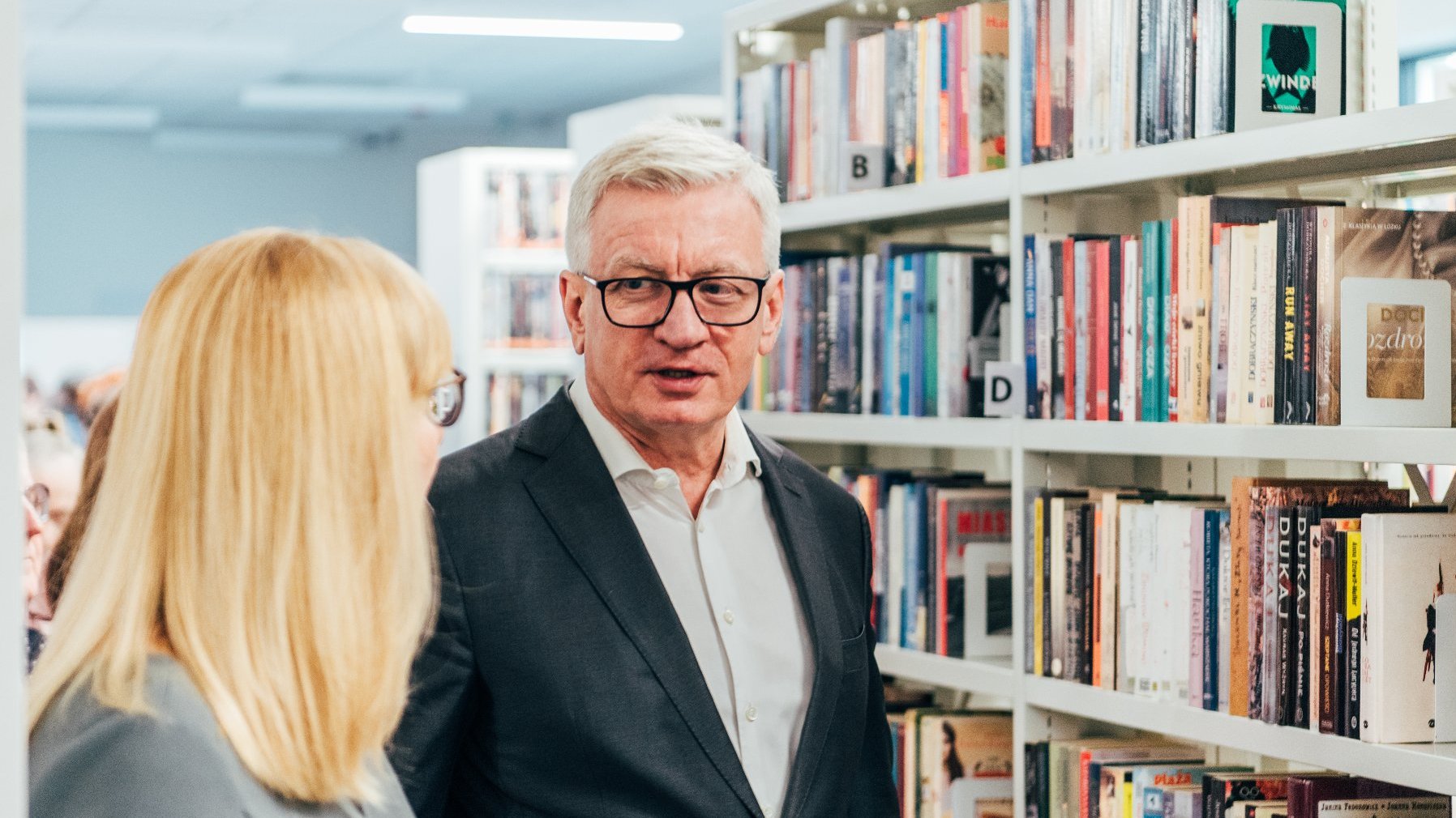 Na zdjęciu prezydent Poznania rozmawia z dyrektorką biblioteki (tyłem), w tle regał z książkami