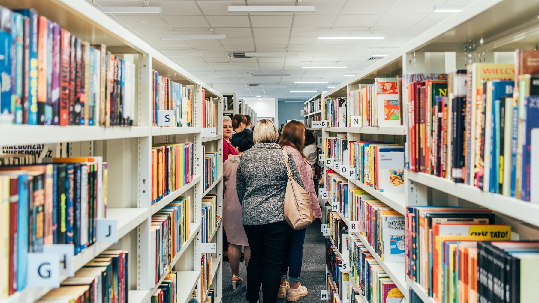 Na zdjęciu regały z książkami, wśród nich czytelnicy