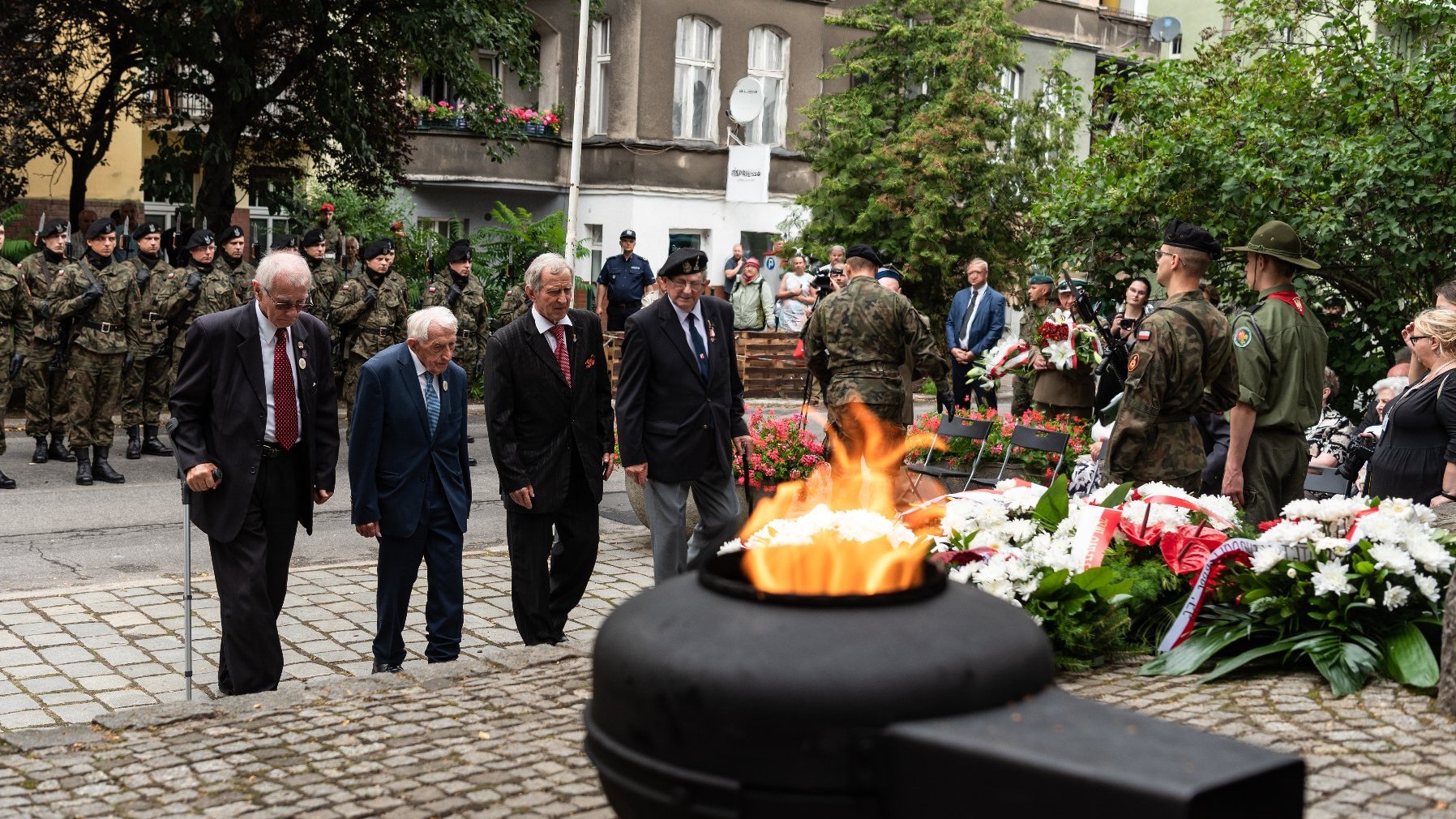 Na zdjęciu delegacja kombatantów składająca kwiaty, na pierwszym planie płonący znicz