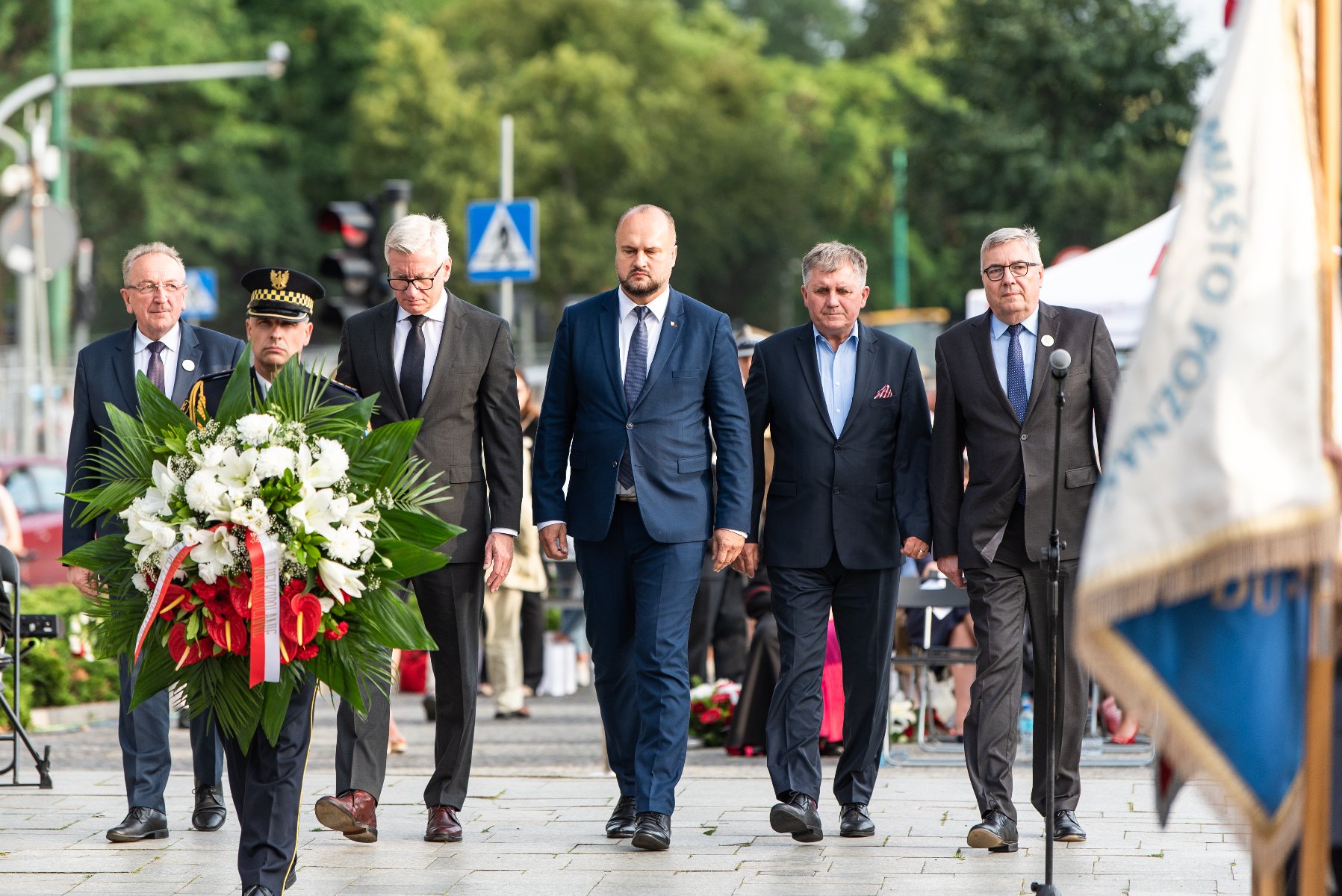 Na zdjęciu przedstawiciele władz Miasta i regionu składają kwiaty pod pomnikiem, na pierwszym planie strażnik z wiązanką - grafika rozmowy