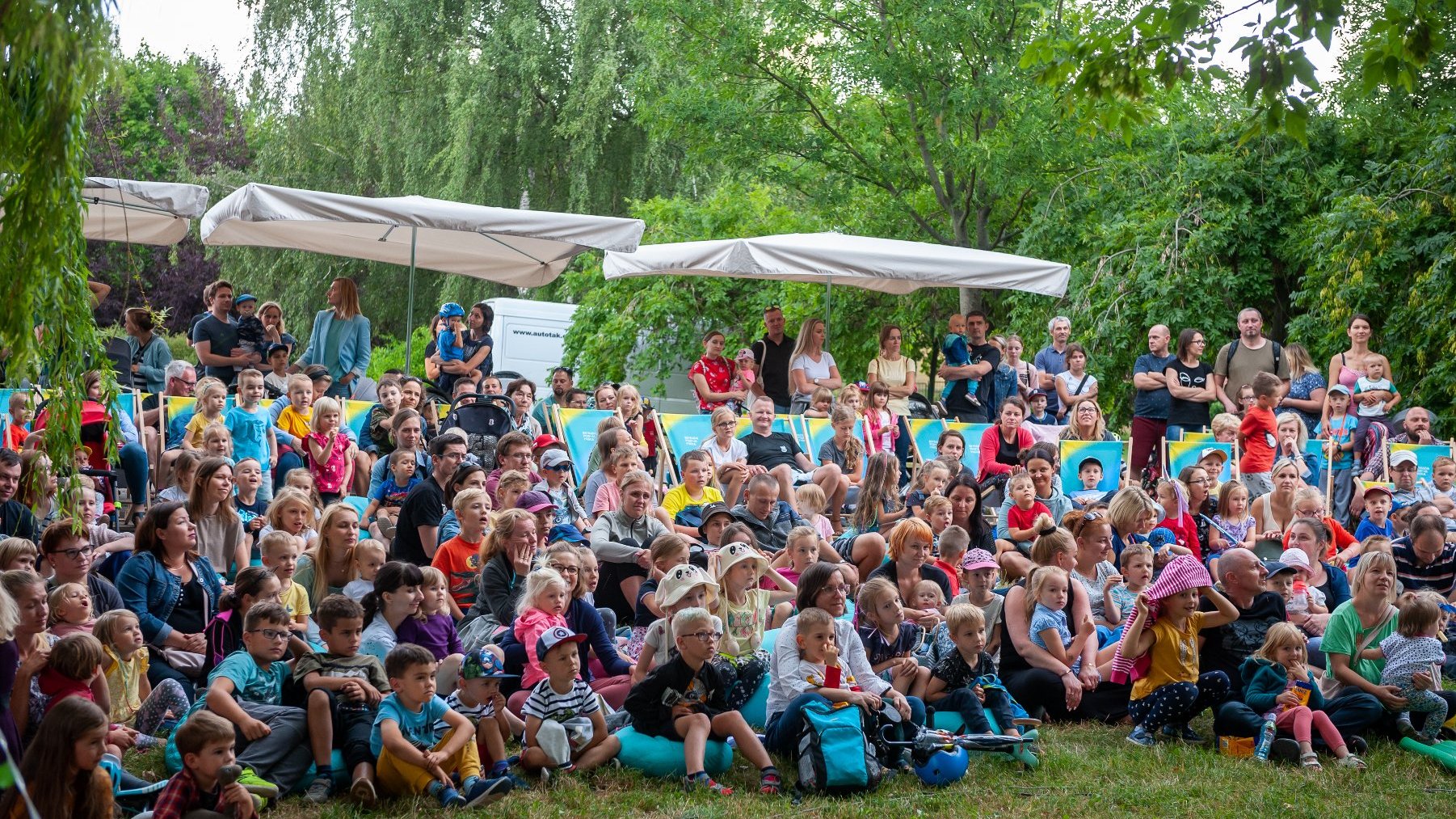 Zdjęcie przedstawia tłum dzieci siedzących na trawie.