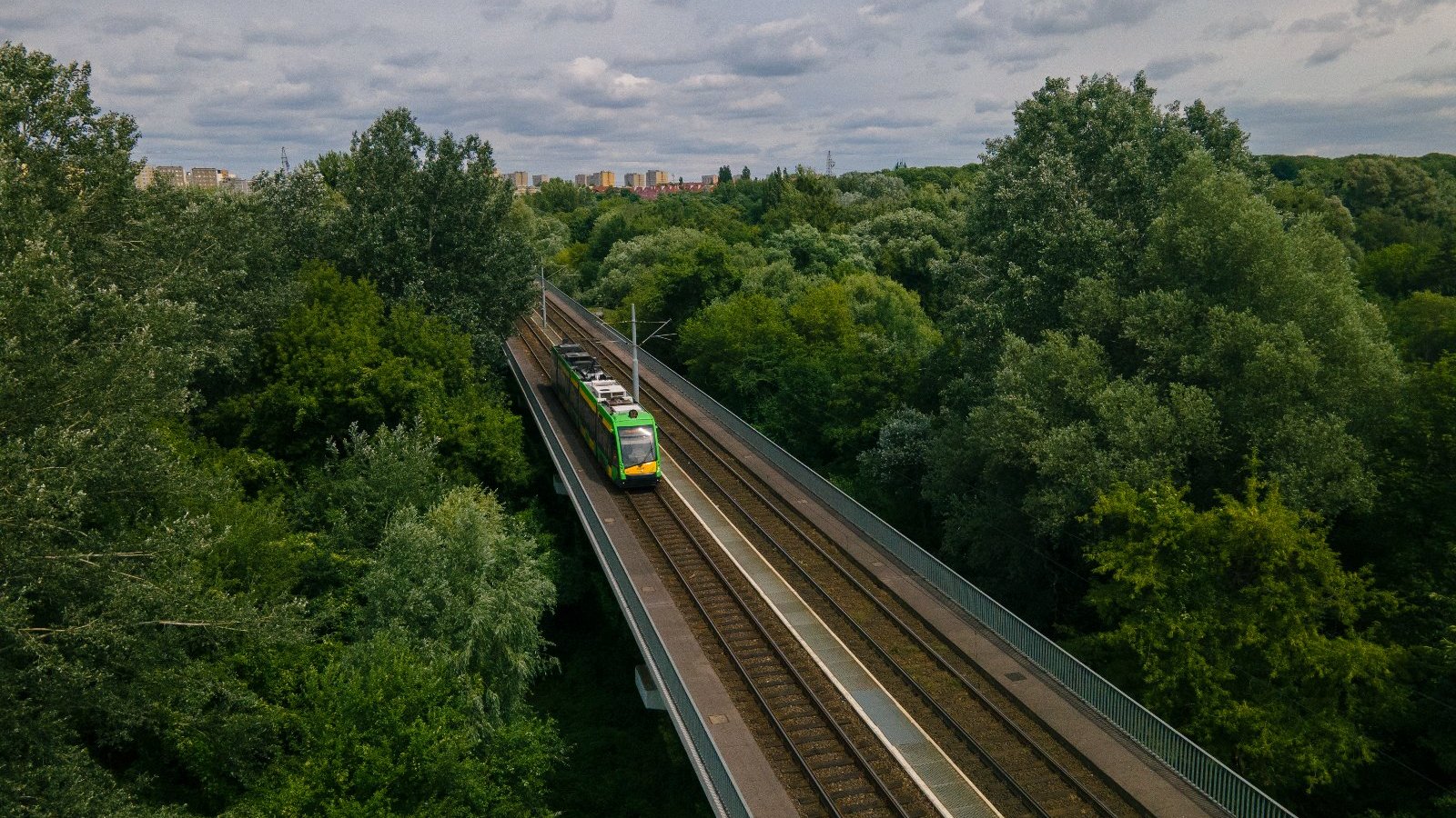 Na zdjęciu trasa PST widziana z lotu ptaka, w centrum tramwaj na torowisku otoczonym drzewami - grafika rozmowy