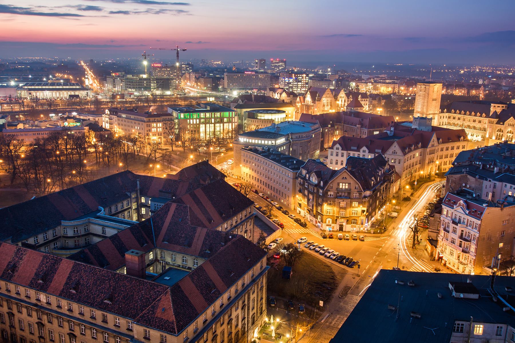 Na zdjęciu panorama Poznania o zmroku, widać dachy kamienic i Okrąglak - grafika rozmowy