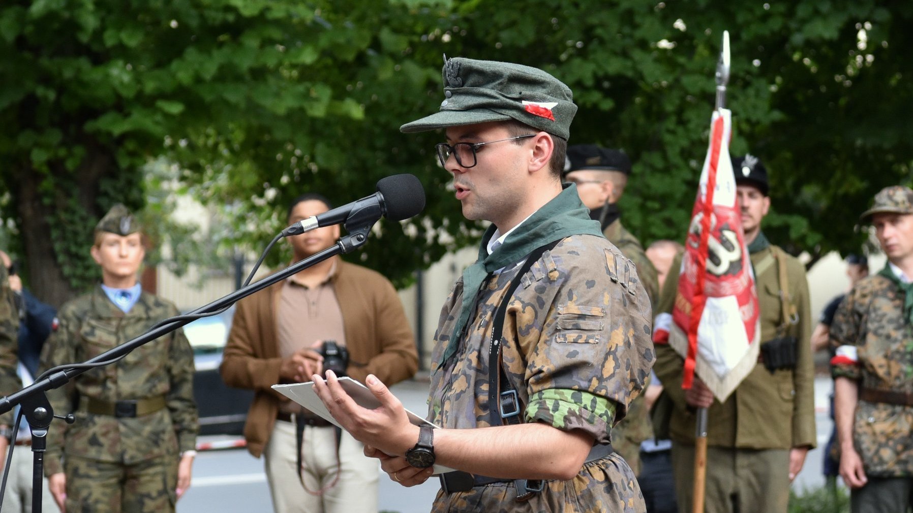 Na zdjęciu młody mężczyzna w mundurze, mówiący do mikrofonu