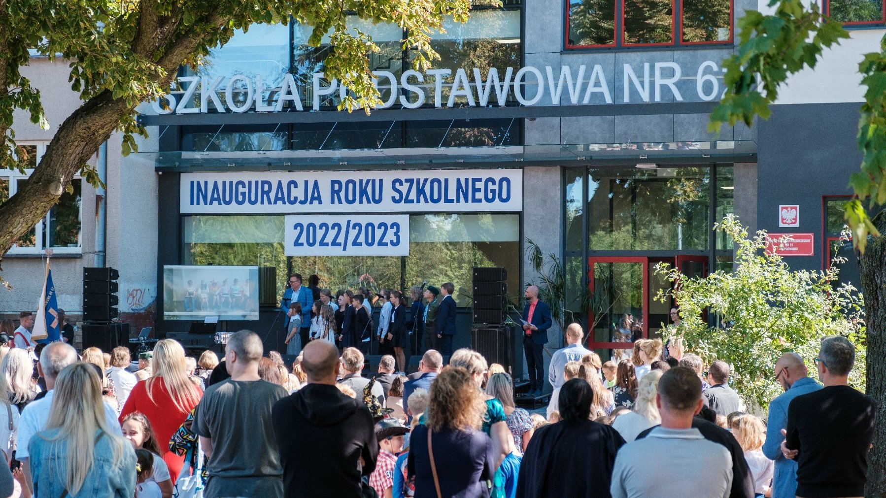 Na zdjęciu budynek szkoły, przed nim grupa ludzi