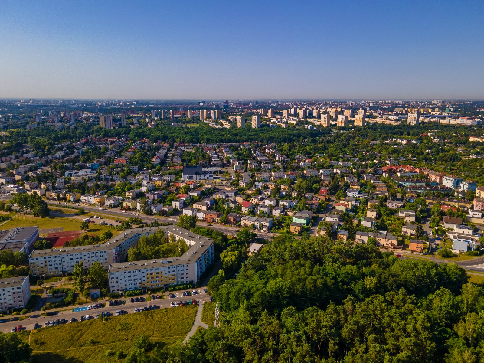 Zdjęcie z lotu ptaka przedstawia zieleń (na dole), obok bloki, później pas domków jednorodzinnych, a dalej bloki mieszkalne - grafika rozmowy