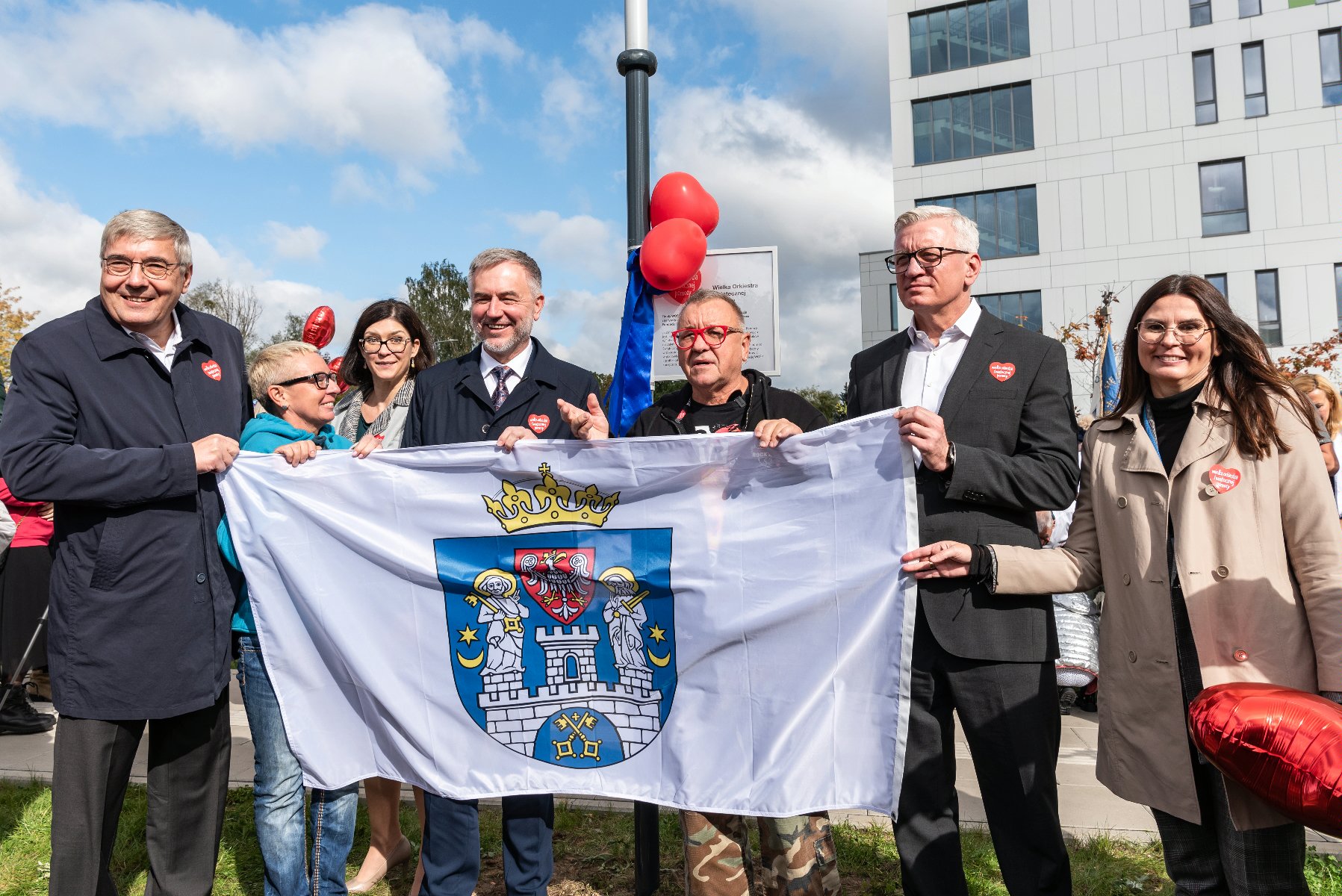 Na zdjęciu samorządowcy oraz Jurek Owsiak, wszyscy trzymają flagę Poznania - grafika rozmowy