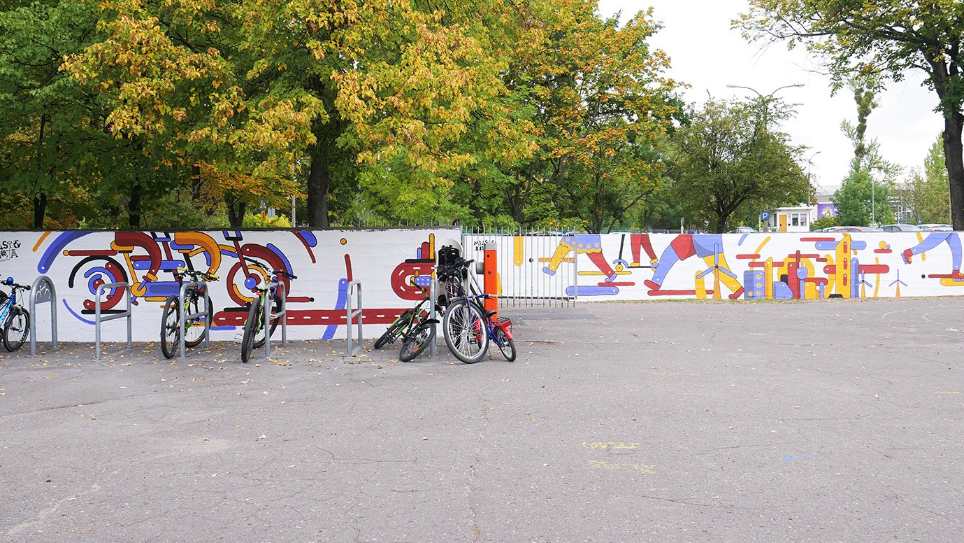 Zdjęcie przedstawia mural wykonany na ogrodzeniu szkoły, przed nim stoją rowery