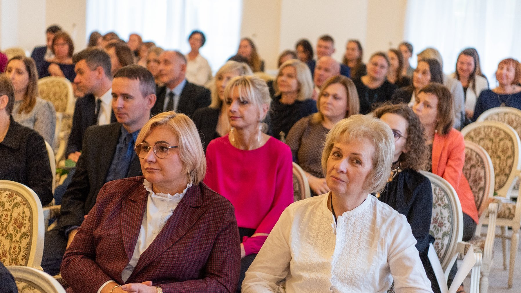 Na zdjęciu grupa ludzi siedząca w sali białej urzędu miasta