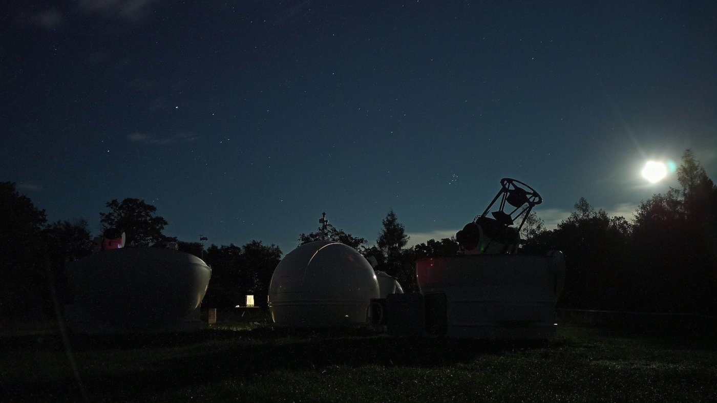 Budynki Obserwatorium Astronomicznego UAM, w tle nocne, rozgwieżdżone niebo.