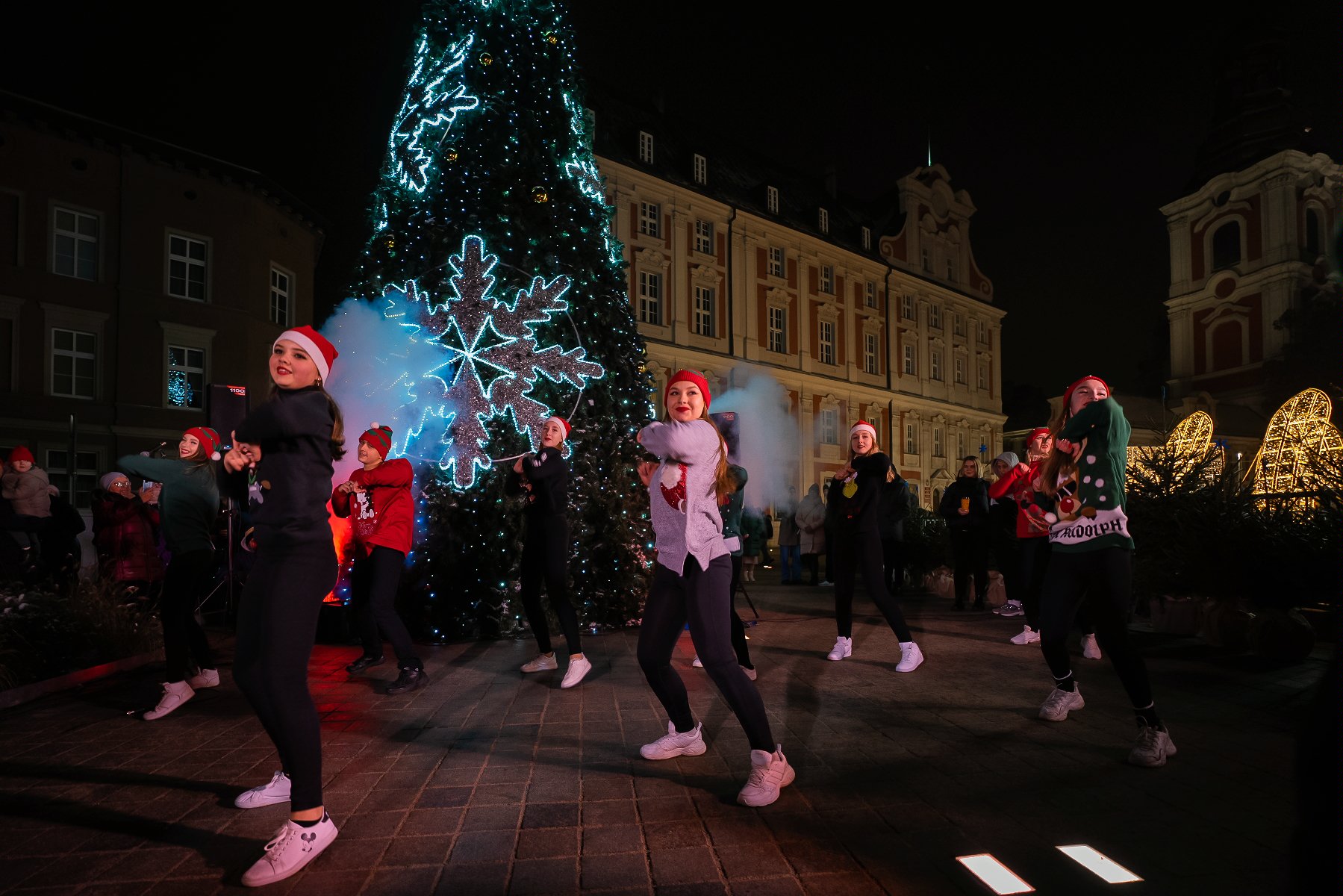 Zdjęcie przedstawia grupę tancerzy w czapkach św. Mikołaja. W tle choinka. - grafika rozmowy