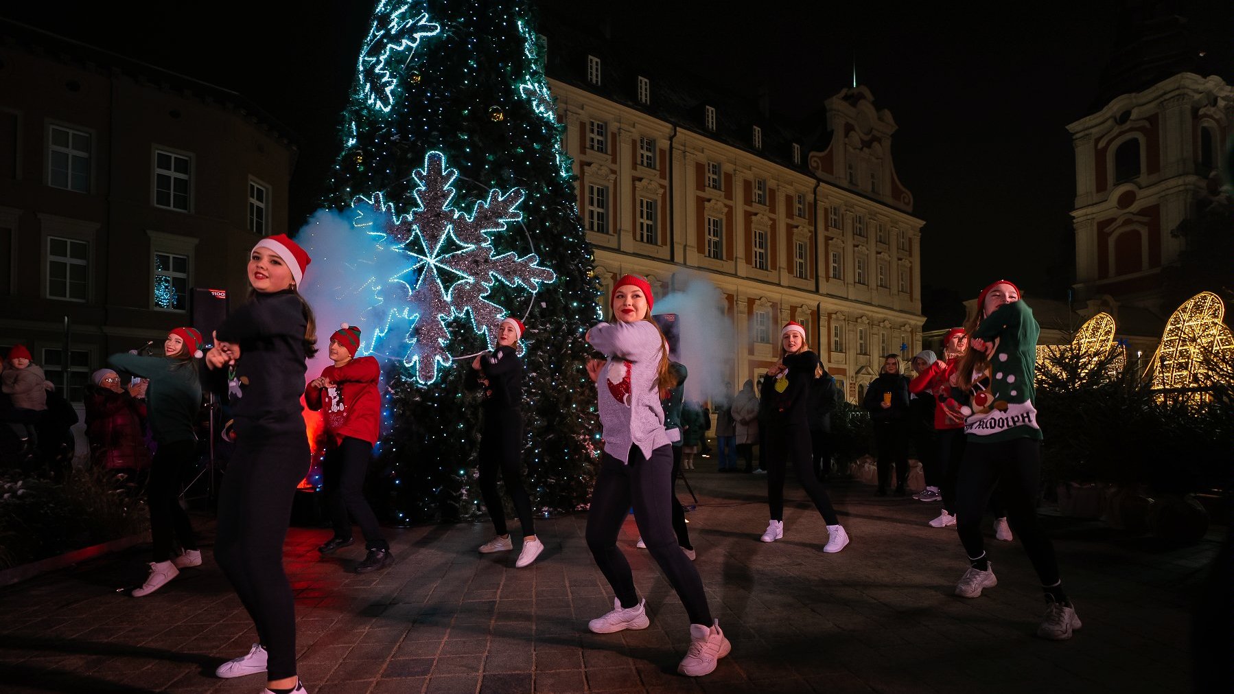 Zdjęcie przedstawia grupę tancerzy w czapkach św. Mikołaja. W tle choinka.