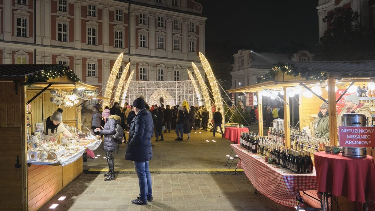 Na zdjęciu ludzi odwiedzający stoiska na jarmarku, w tle iluminacje