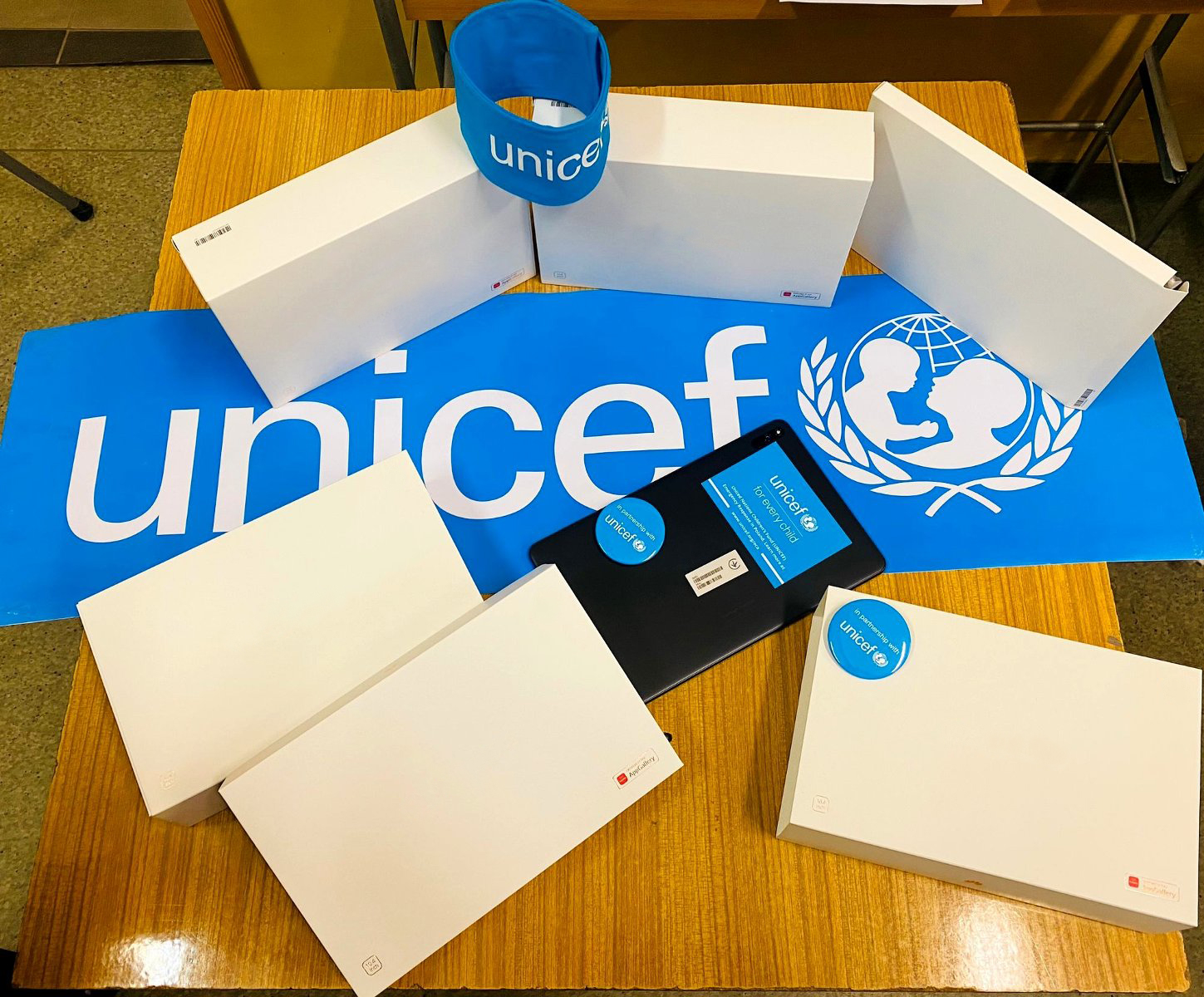 Na zdjęciu tablety - większość w pudełkach - leżące na na stole, obok logo UNICEF - grafika rozmowy