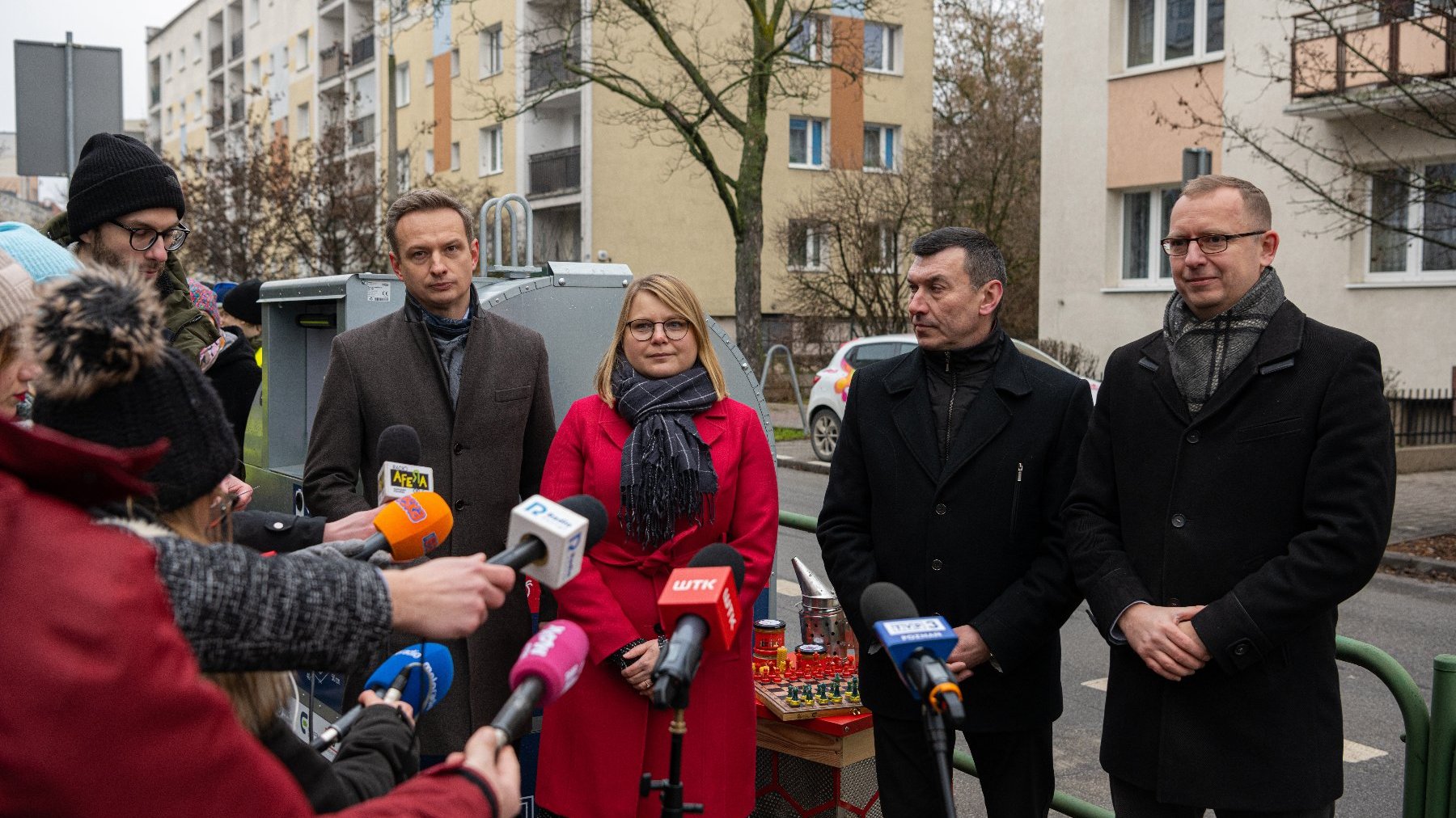 Na zdjęciu trzech mężczyzn i kobieta, obok nich dziennikarze z mikrofonami, w tle pojemnik na odpady