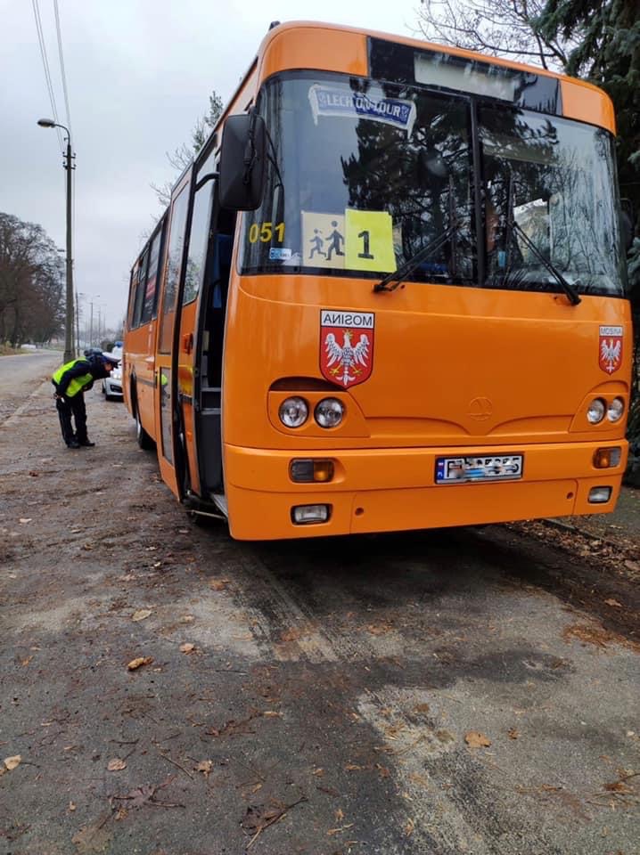 Na zdjęciu policjant przyglądający się tylnej oponie autobusu - grafika rozmowy