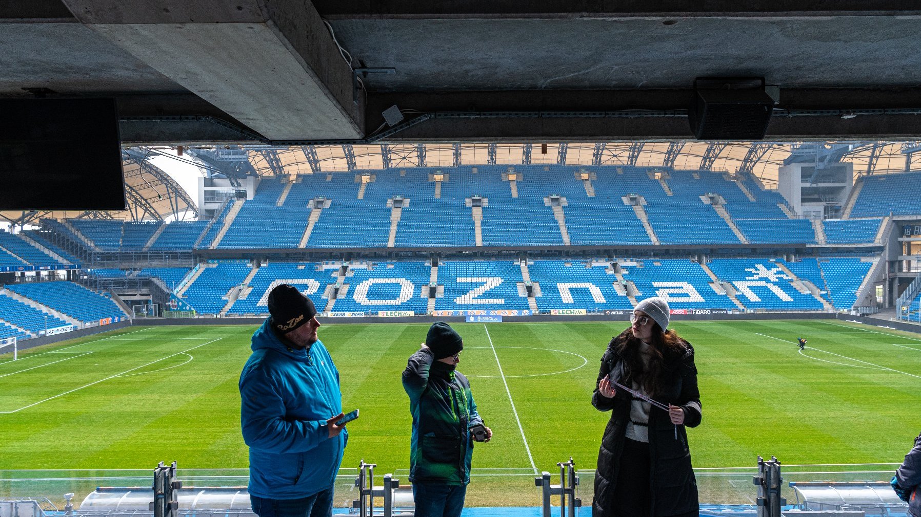 Na zdjęciu trzy osoby, w tle trybuny stadionu