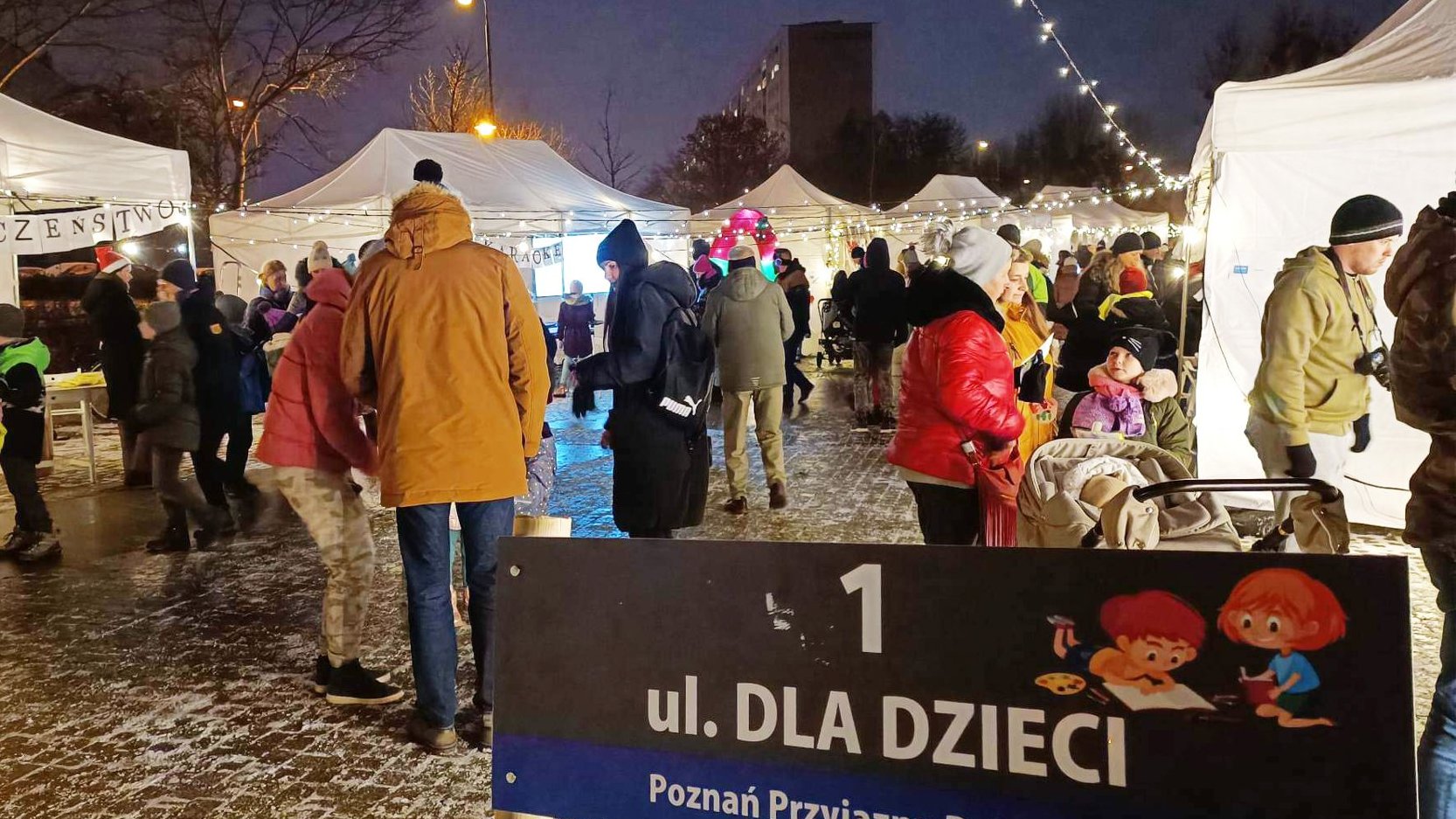 Na zdjęciu oświetlone namioty, pomiędzy nimi widać dużo dzieci i ich opiekunów