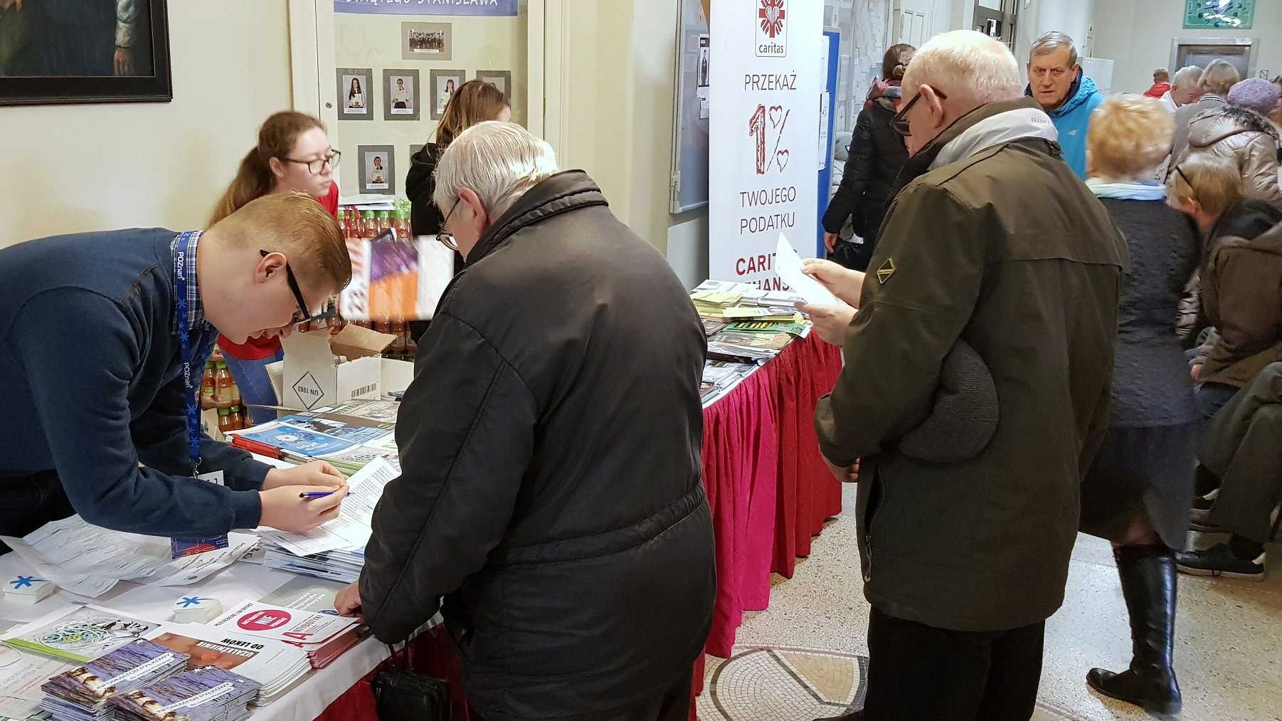 Na zdjęciu ludzie w szkolnym korytarzu, widać stoiska - grafika rozmowy