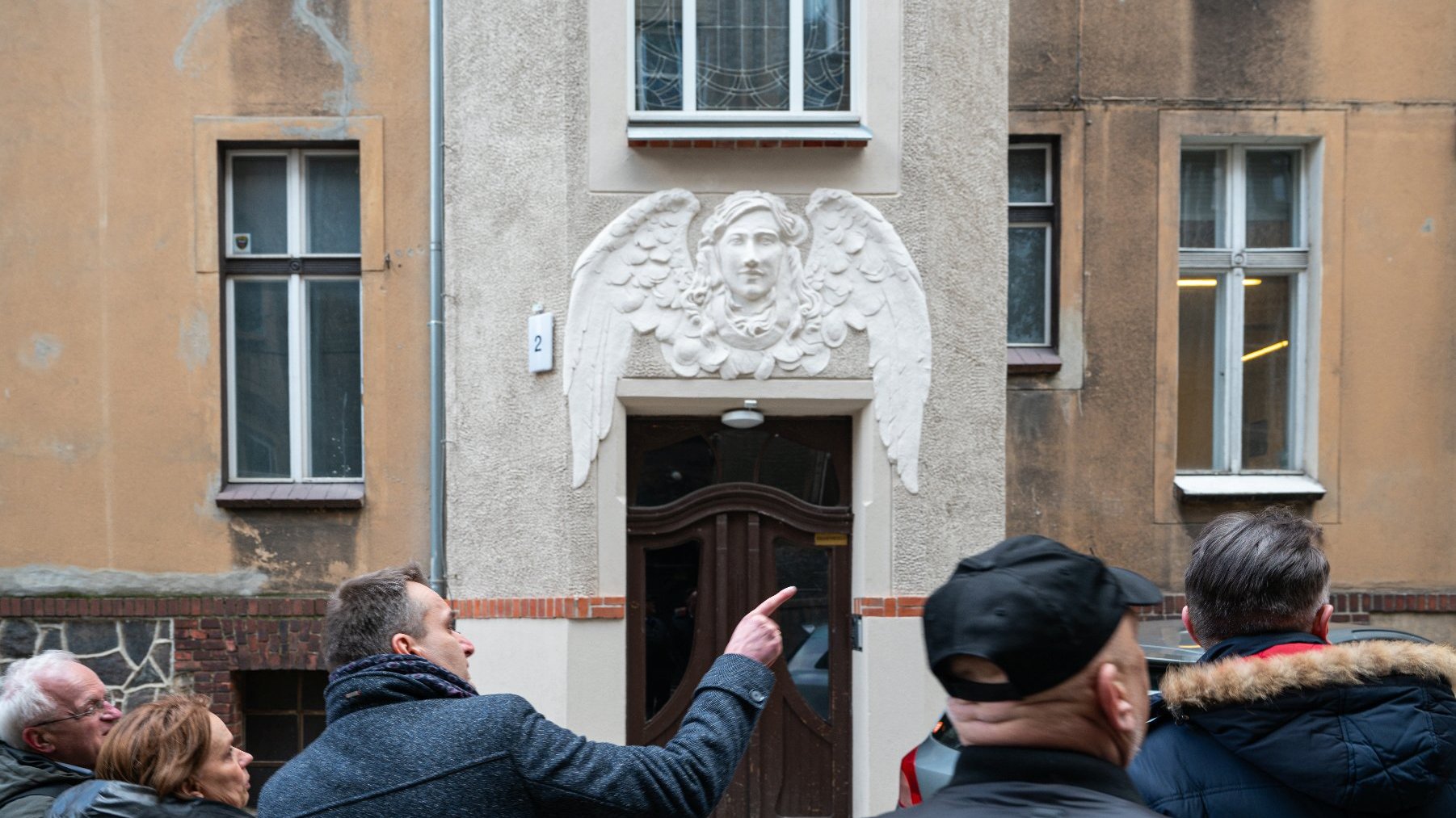 Na zdjęciu kilka osób patrzących na detal kamienicy