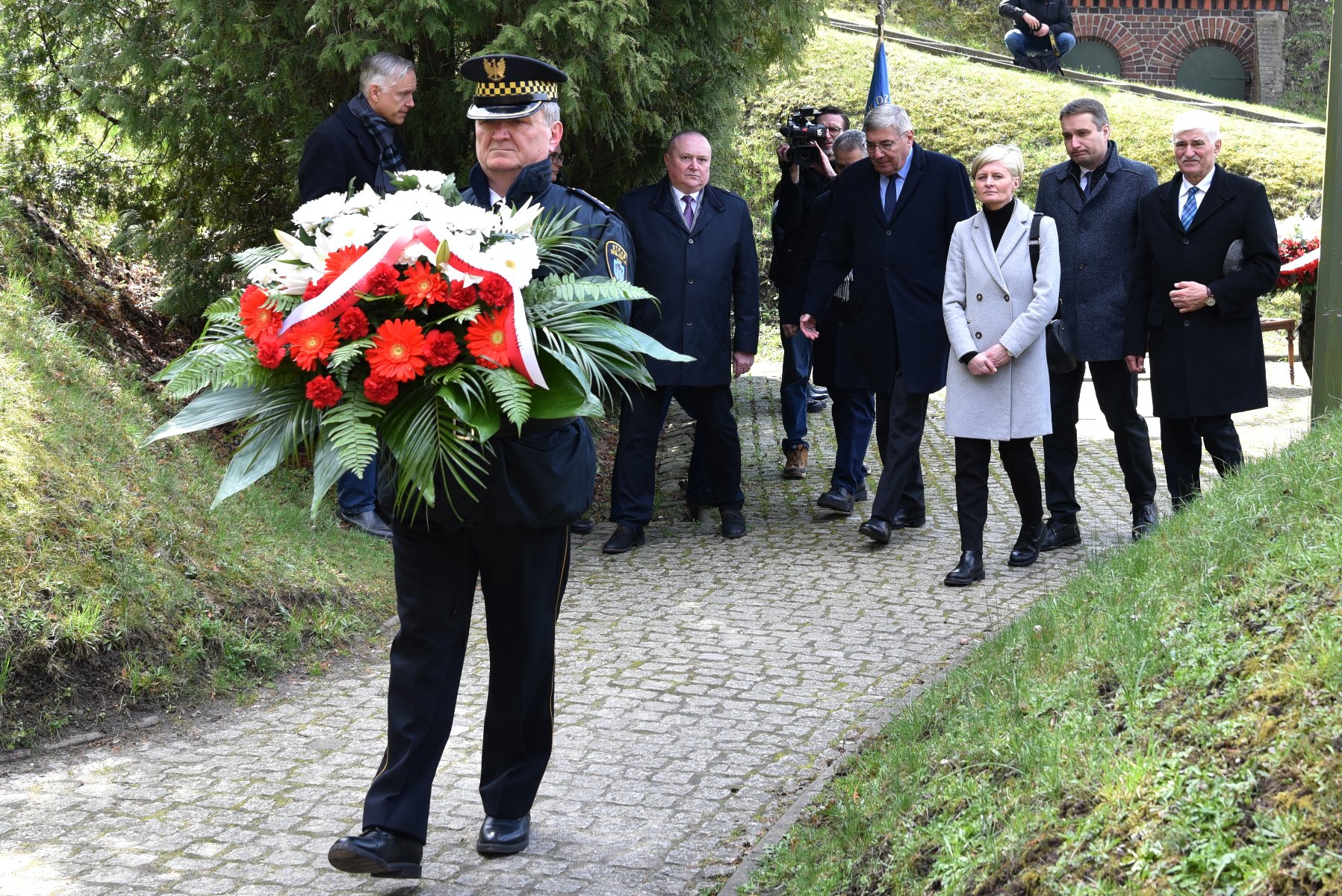 Na zdjęciu grupa osób składających wieniec z kwiatów - grafika rozmowy