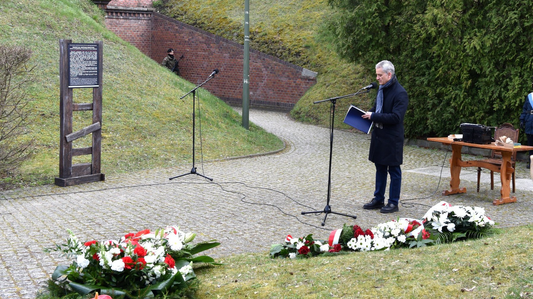 Na zdjęciu dyrektor muzeum przy mikrofonie, w pobliżu widać leżące wiązanki kwiatów