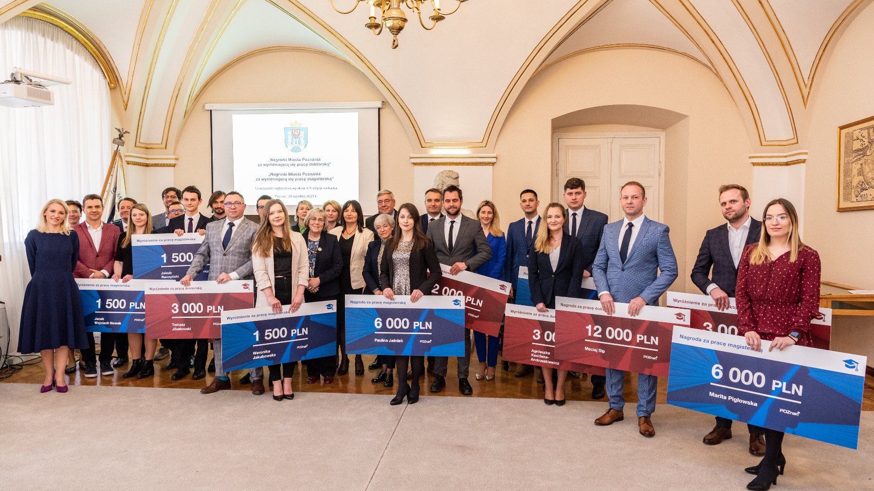 Na zdjęciu grupa ludzi - nagrodzeni - pozuje do zdjęcia z symbolicznymi czekami