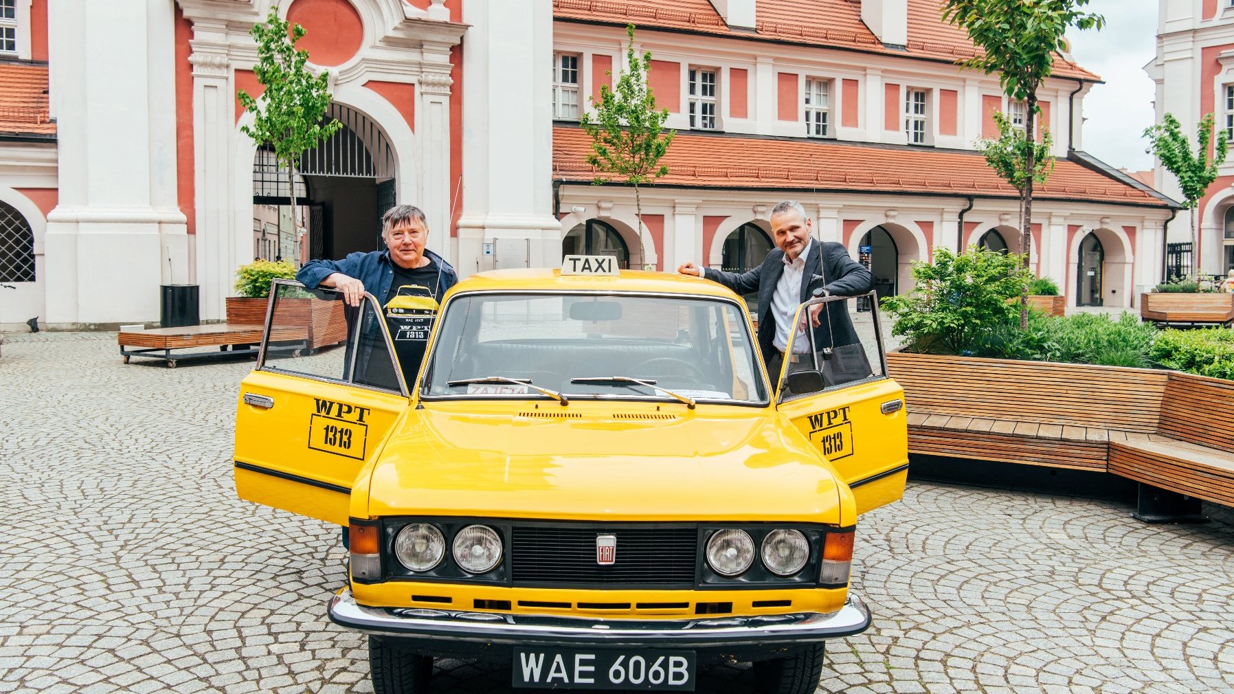 Galeria zdjęć z konferencji na dziedzińcu urzędu miasta, na zdjęciach żółta taksówka z serialu "Zmiennicy", aktor oraz zastępca prezydenta Poznania