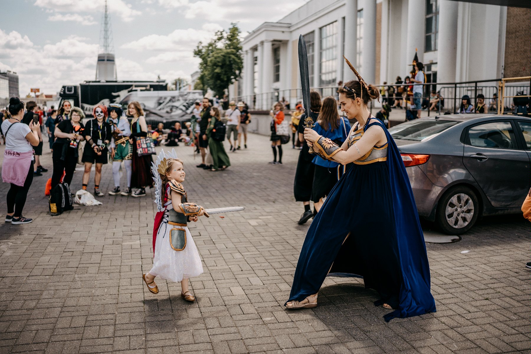 Na pierwszym planie przebrana mama z córką. W tle inni cosplajowcy na terenie MTP - grafika rozmowy