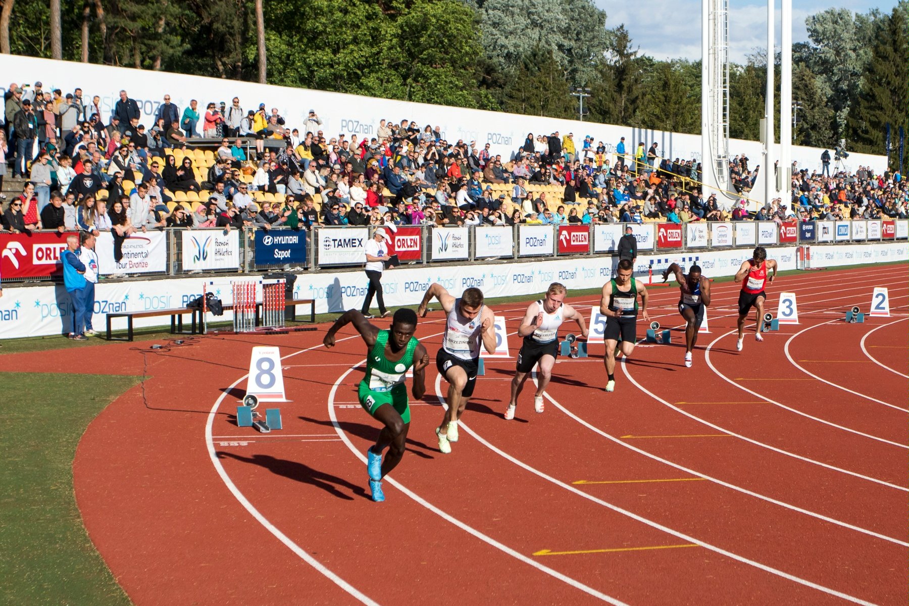 Start zawodników w biegu na 200 metrów. W tle publiczność na trybunach stadionu na Golęcinie - grafika rozmowy