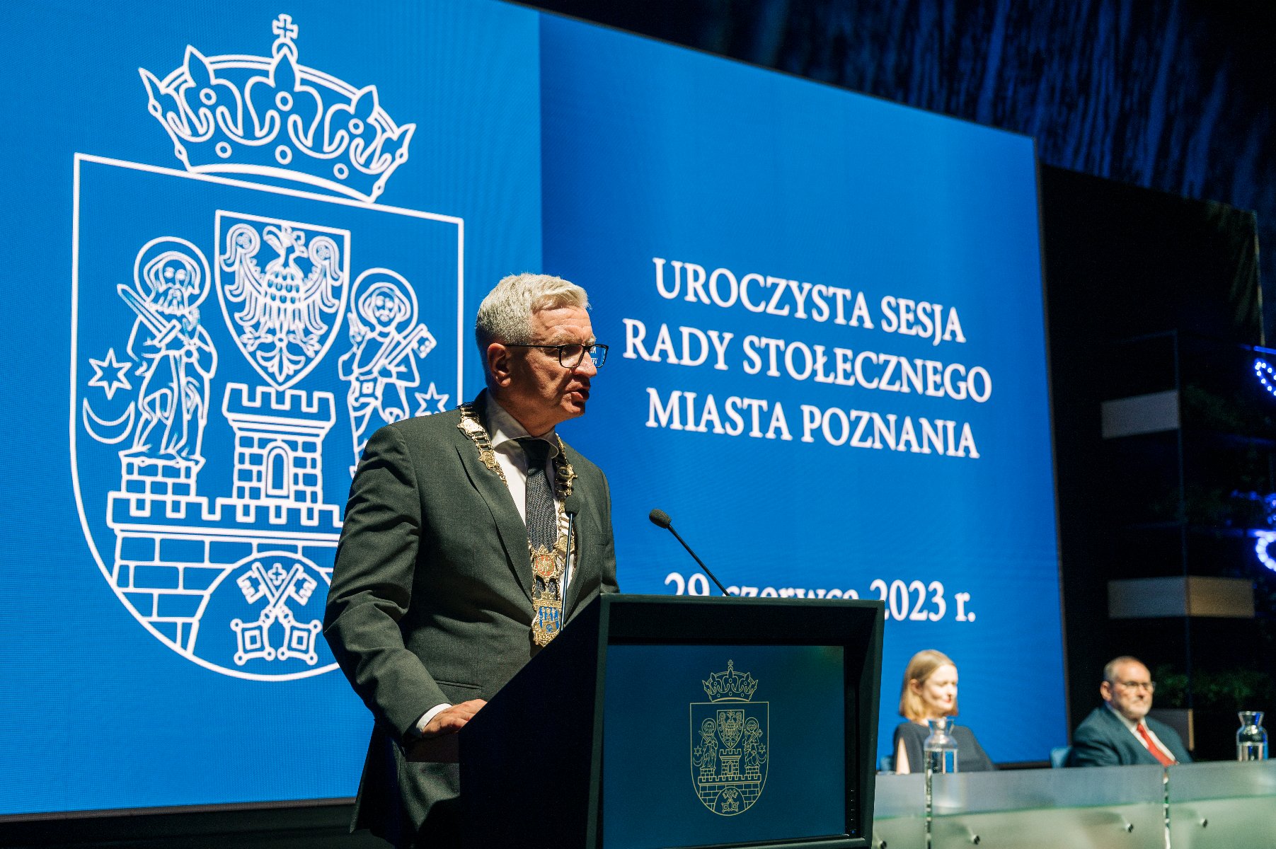 Na zdjeciu prezydent Poznania przy mikrofonie, w tle napis: uroczysta sesja rady stołecznego miasta Poznania - grafika rozmowy