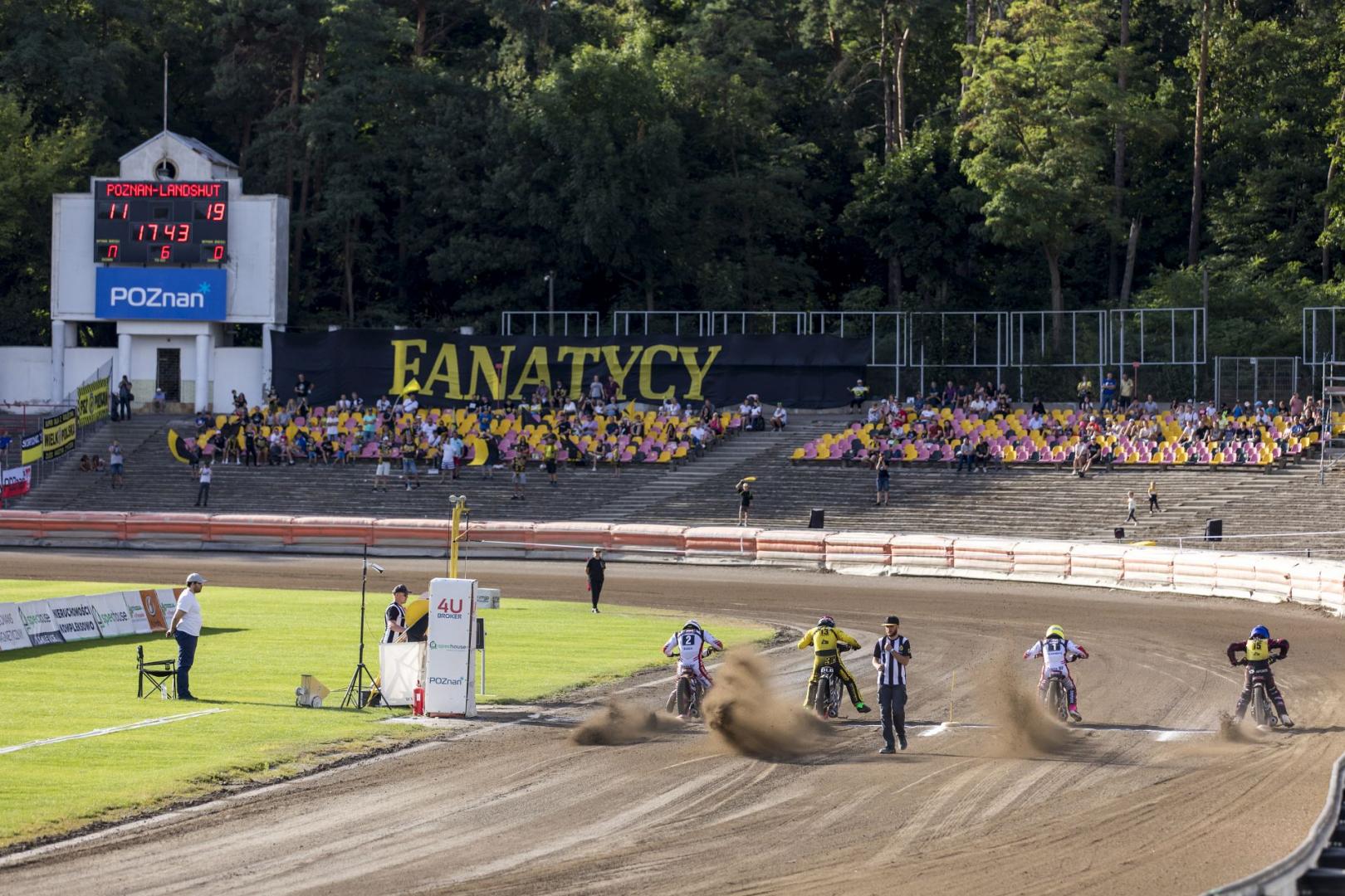 Na zdjęciu widać stadion żużlowy na Golęcinie, startujących żużlowców i kibiców na trybunach - grafika rozmowy