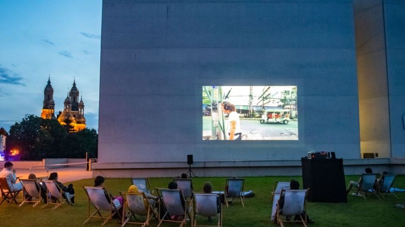 Na zdjeciu ludzie leący na leżakach i oglądający film na świeżym powietrzu