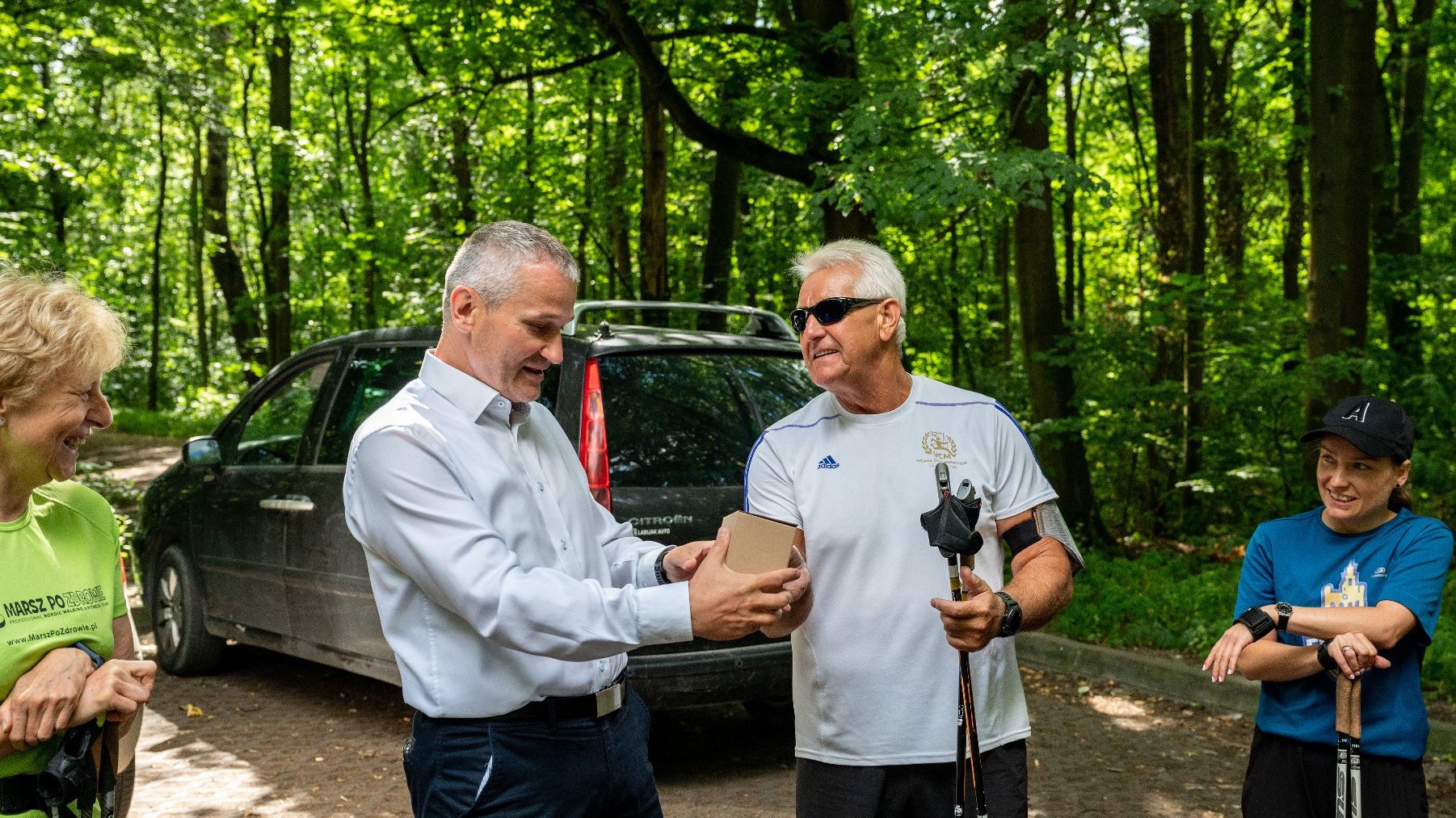 Galeria zdjęć przedstawia grupę seniorów w strojach sportowych z kijkami do nordic walking.