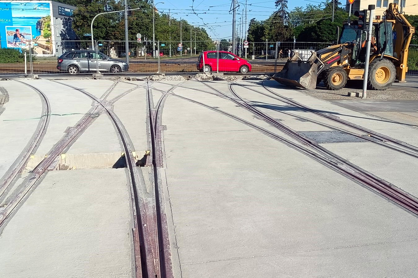 Na zdjęciu zbliżenie na łuki szyn tramwajowych, w tle widać koparkę i samochody - grafika rozmowy