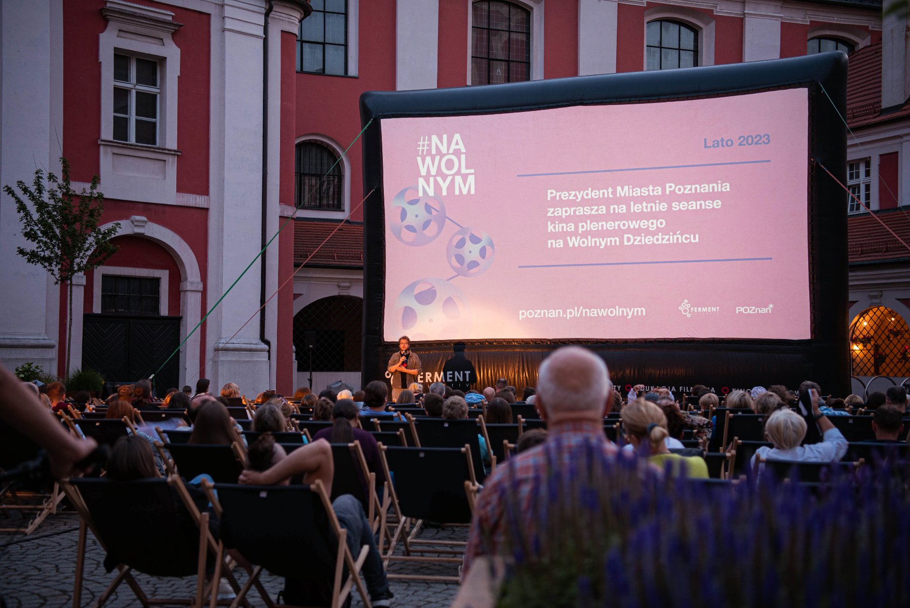 na zdjęciu ludzie zebrani na Wolnym Dziedzińcu oglądają kino plenerowe - grafika rozmowy