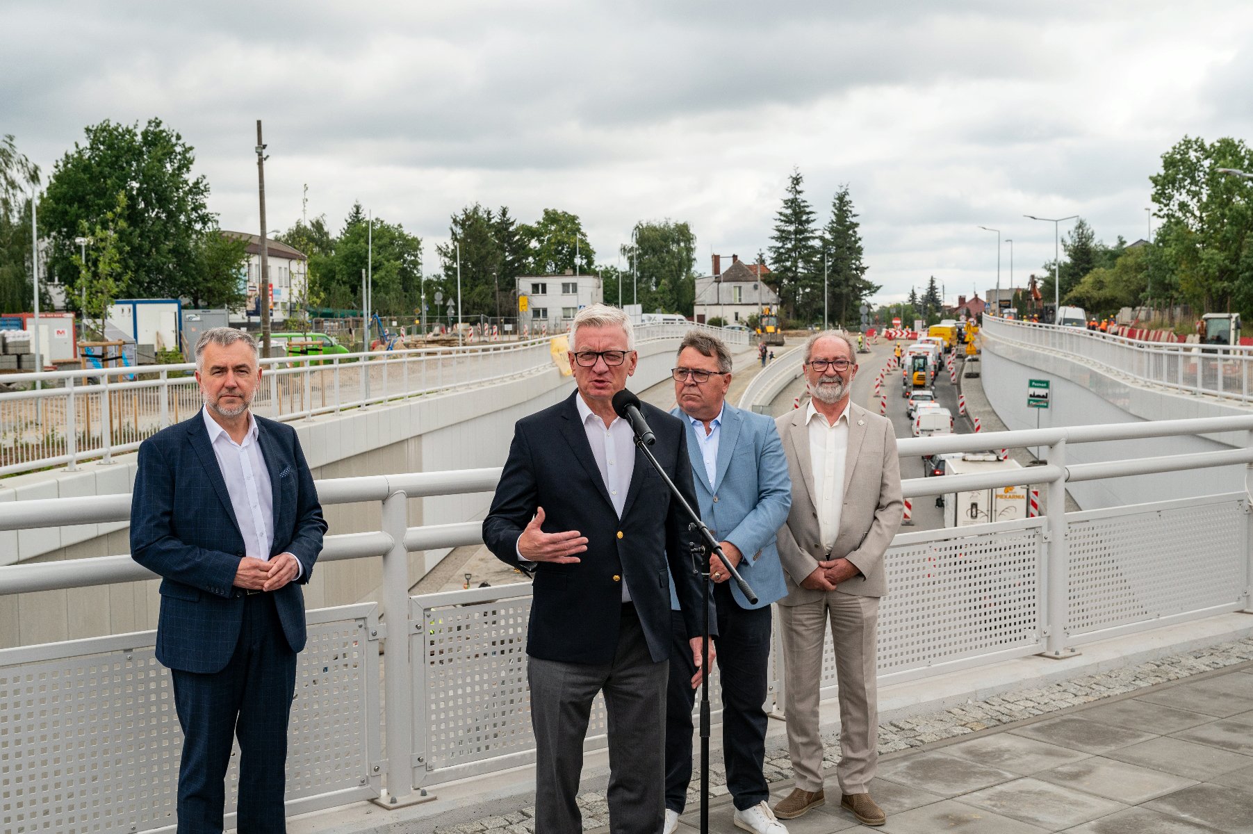 Na zdjęciu czterej mężczyźni, za nimi przejazd pod torami - grafika rozmowy