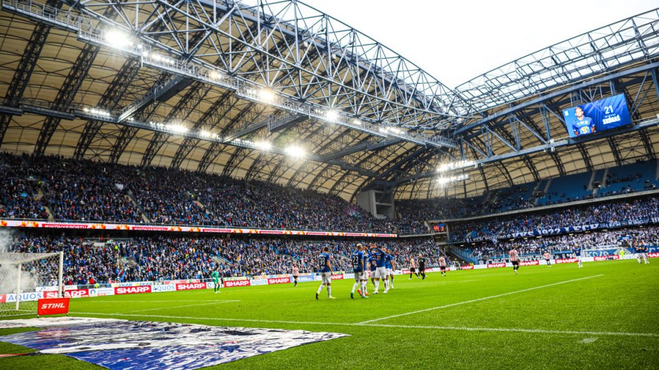 Zdjęcie przedstawia stadion Lecha. Na pierwszym planie widać piłkarzy na murawie w tle trybuny.