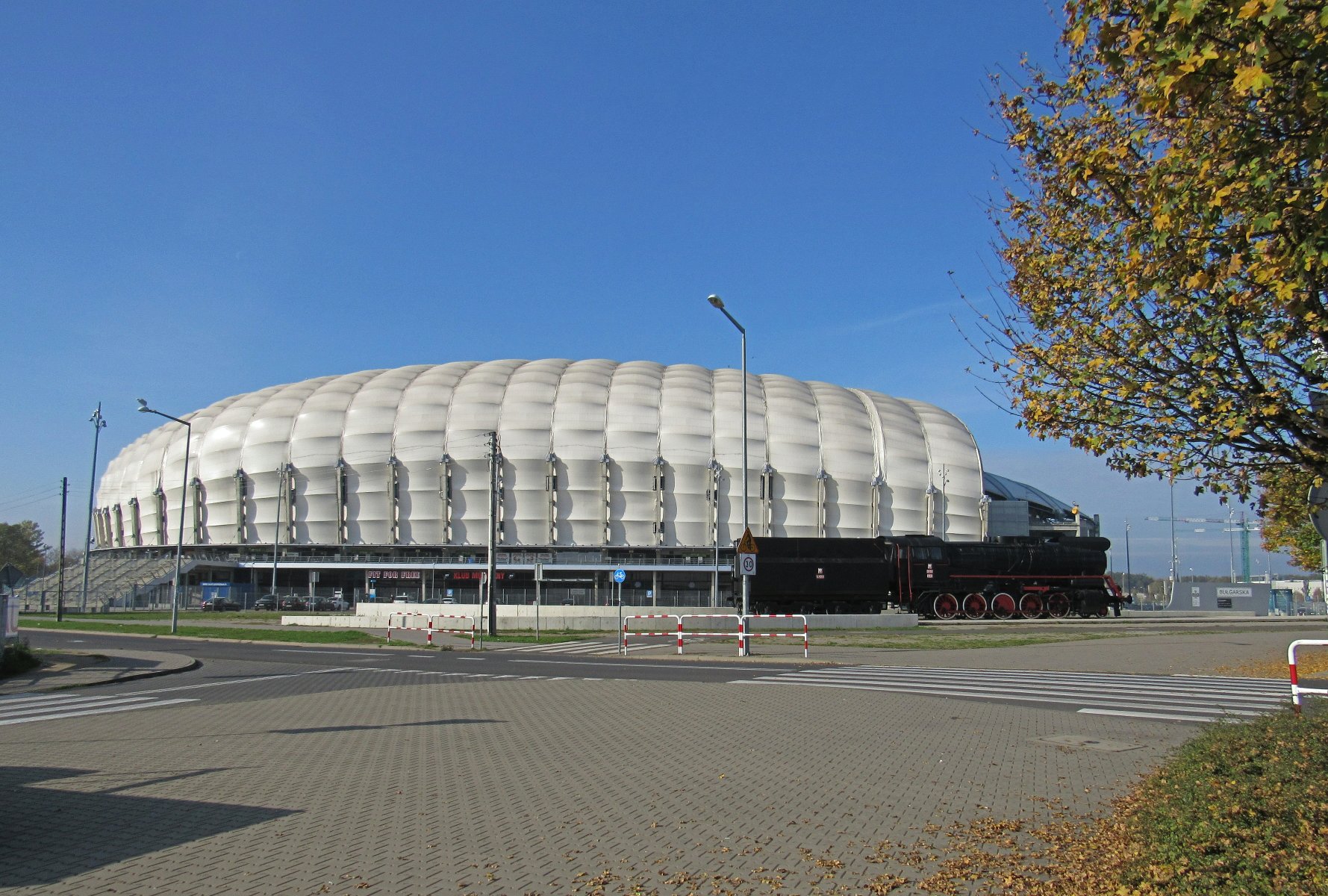 Zdjęcie przedstawia białą kopułę stadionu przy ul. Bułgarskiej. Przed nim stoi parowóz. - grafika rozmowy