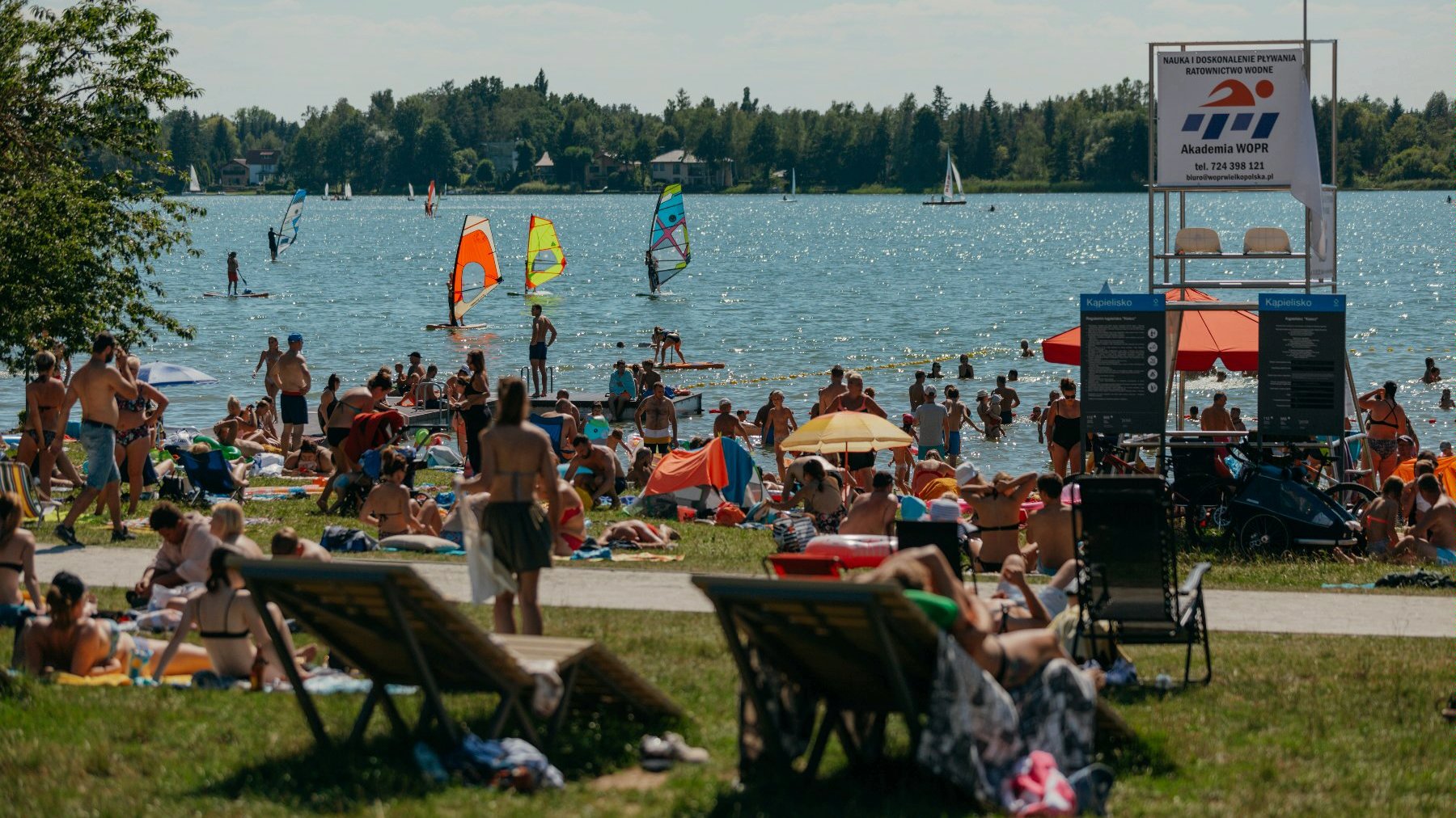 Na zdjęciu tłum ludziplazujących nad brzegiem jeziora - grafika rozmowy