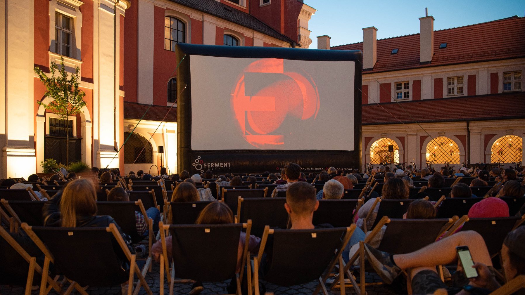 Na zdjęciu ludzie na leżakach oglądają film