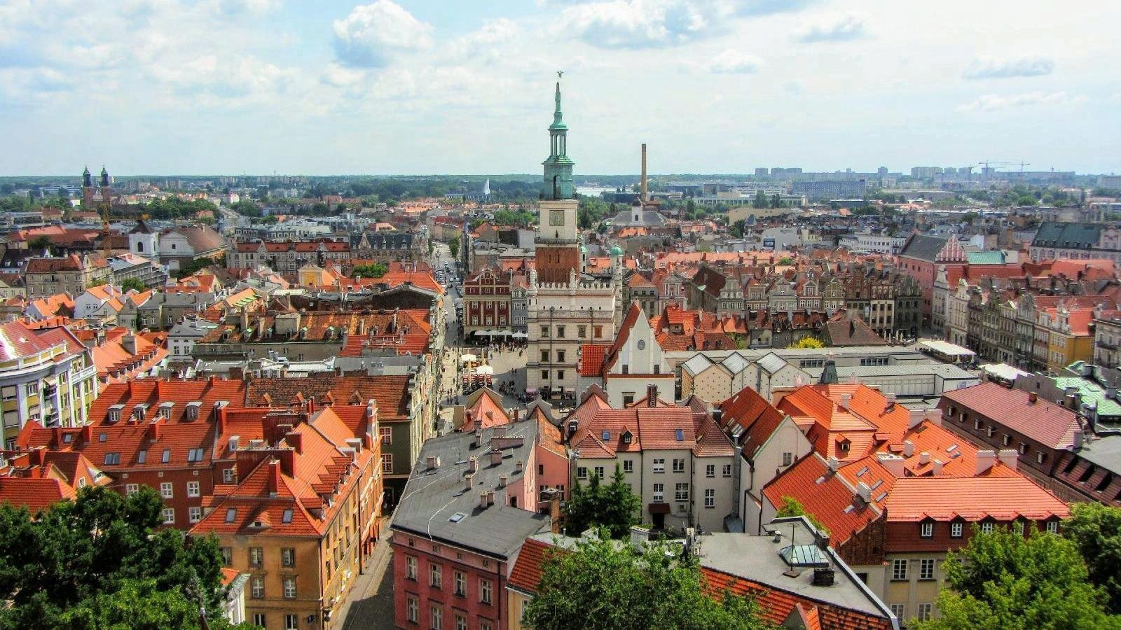 Stary Rynek widziany z lotu ptaka. Na środku kadru widać więżę ratusza, w otoczeniu czerwonych dachów kamienic.