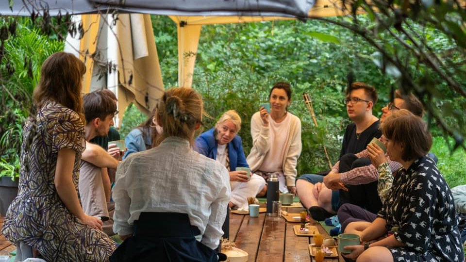 Na zdjęciu ludzie siedzący przy stoliku, piją herbatę i rozmawiają