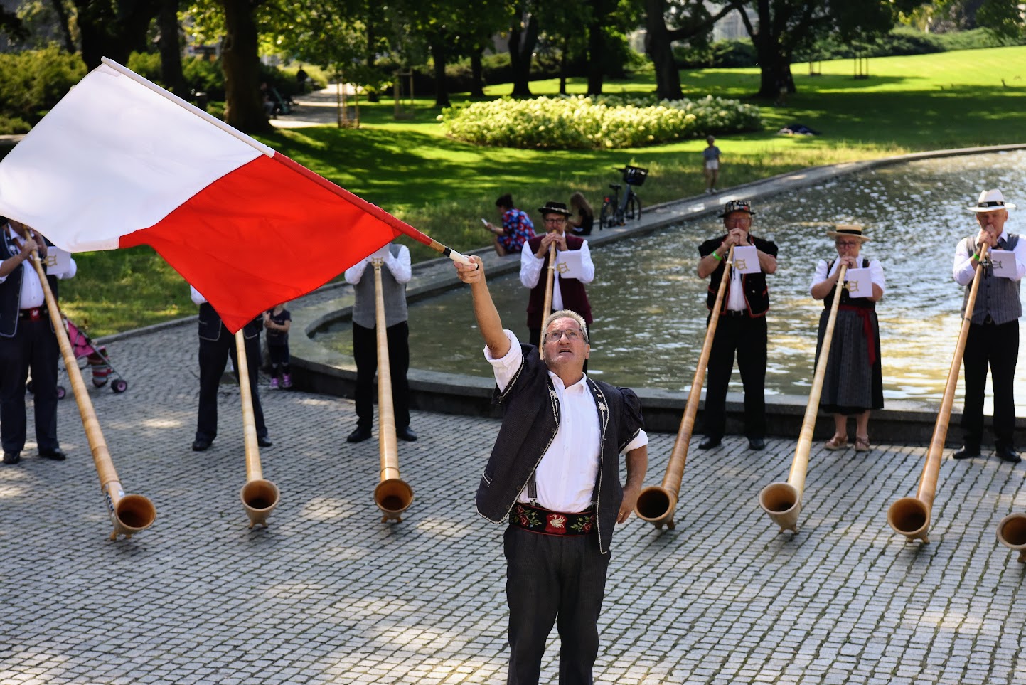 Na zdjęciu mężczyzna z flagą Polski, za nim muzycy grający na rogach - grafika rozmowy