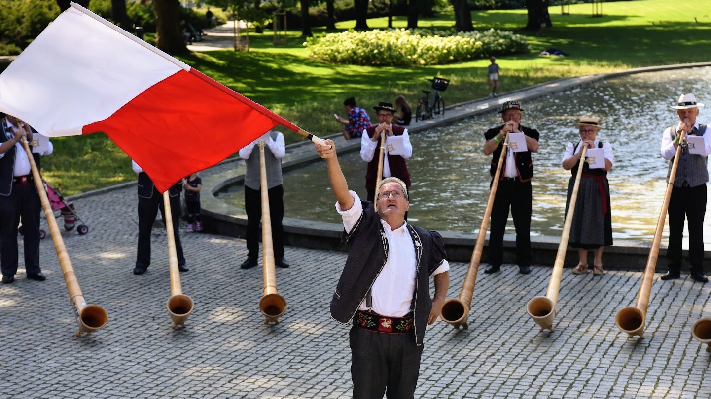 Na zdjęciu mężczyzna z flagą Polski, za nim muzycy grający na rogach