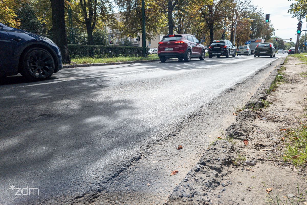 Zniszczona nawierzchnia ul. Reymonta i jadące po niej samochody - grafika rozmowy