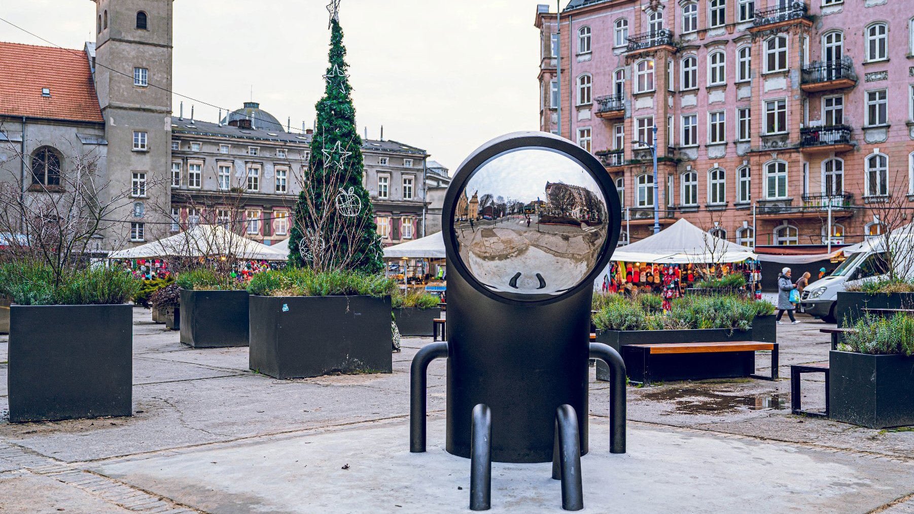 Na zdjęciu rzeźba Watchera widziana z przodu, w tle rynek