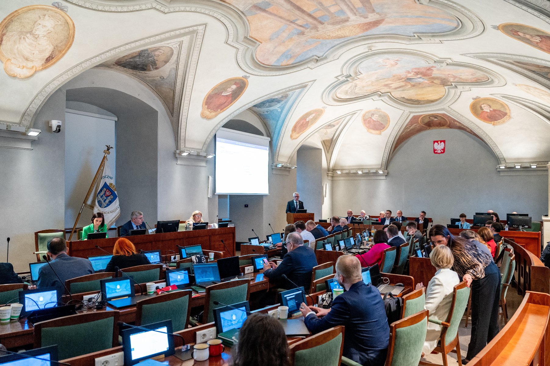 Na zdjeciu sala sesyjna, w niej radni, za mównicą prezydent Poznania - grafika rozmowy