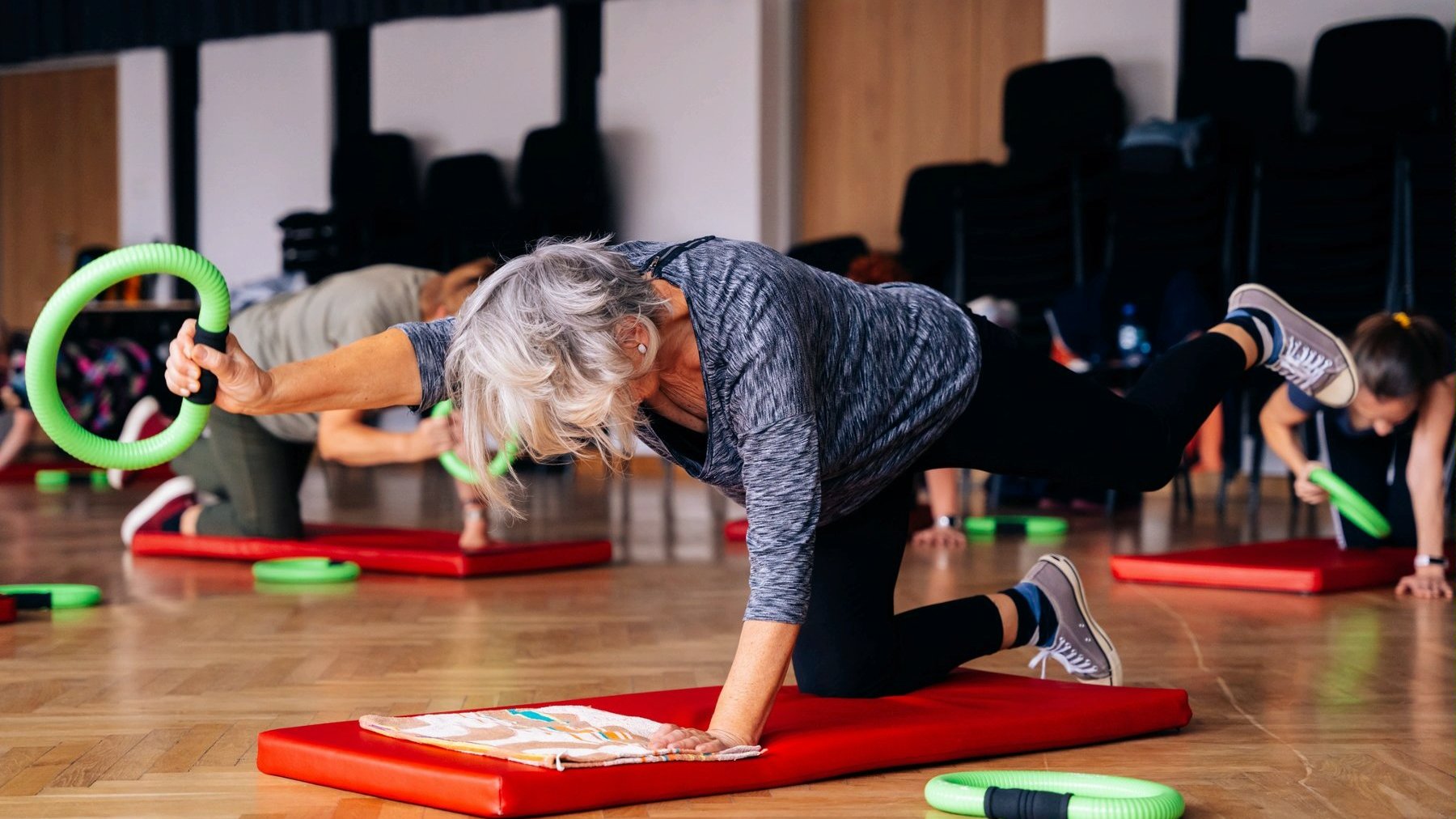 Zdjęcie przedstawia seniorkę wykonującą ćwiczenia na macie. - grafika rozmowy