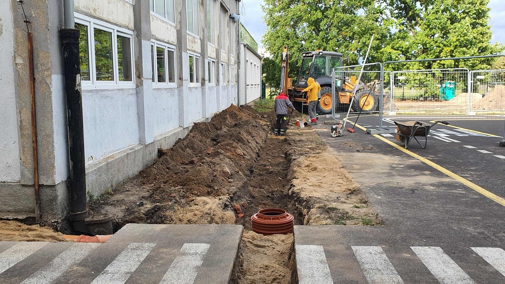 Zdjęcie przedstawia prace budowlanej. Widać na nim m.in. dziurę w ziemi i pracowników budowlanych.